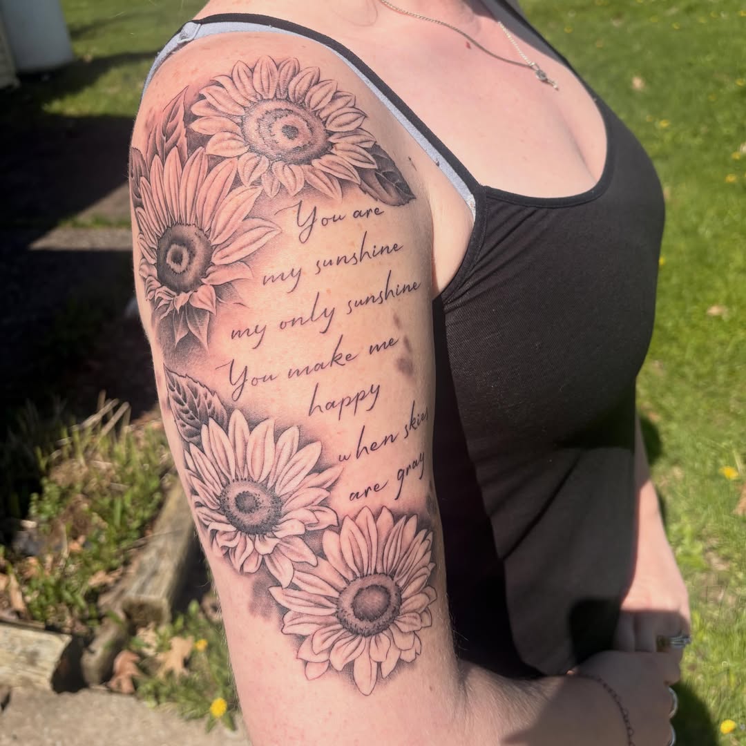 Sunflowers and quote black and grey tattoo on the upper arm by Adriana Wimler