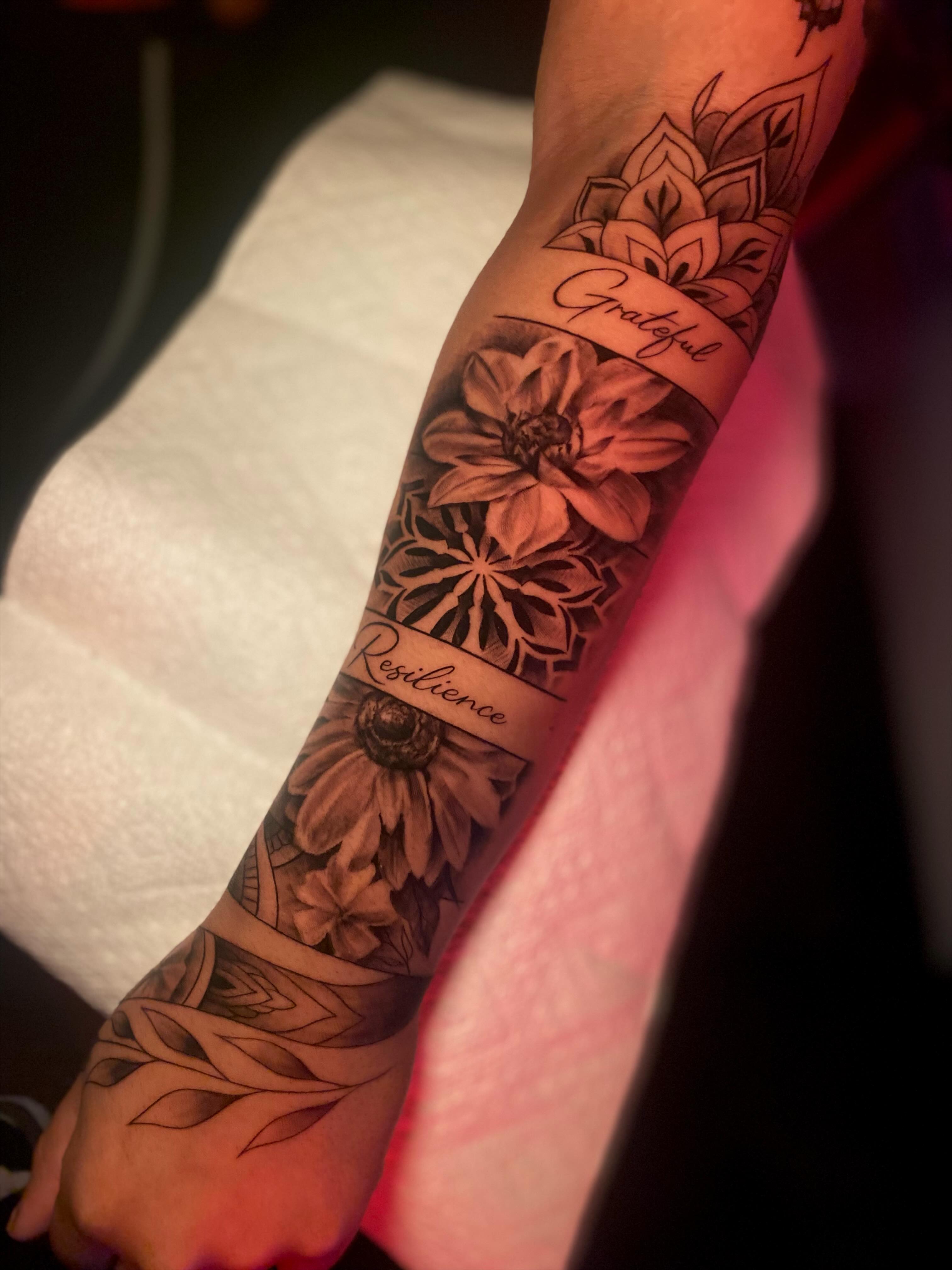Flowers and lettering black and grey tattoo on the forearm by Tattoo Artist