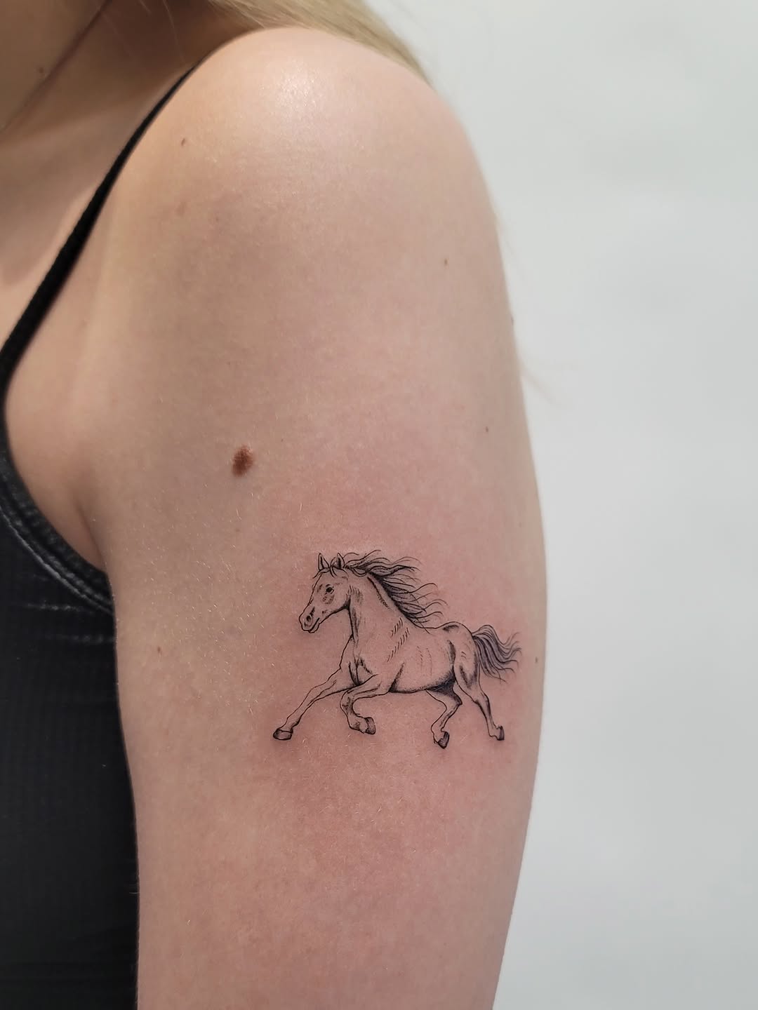 Running horse minimalist tattoo on the upper arm by Las Vegas Fine Line Tattoos