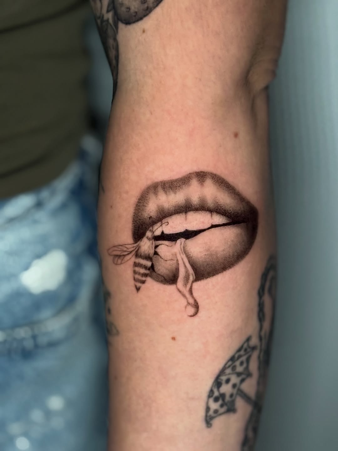 Lips with a bee surrealism tattoo on the forearm by Jojo Rose ✨ Denver Tattoo Artist