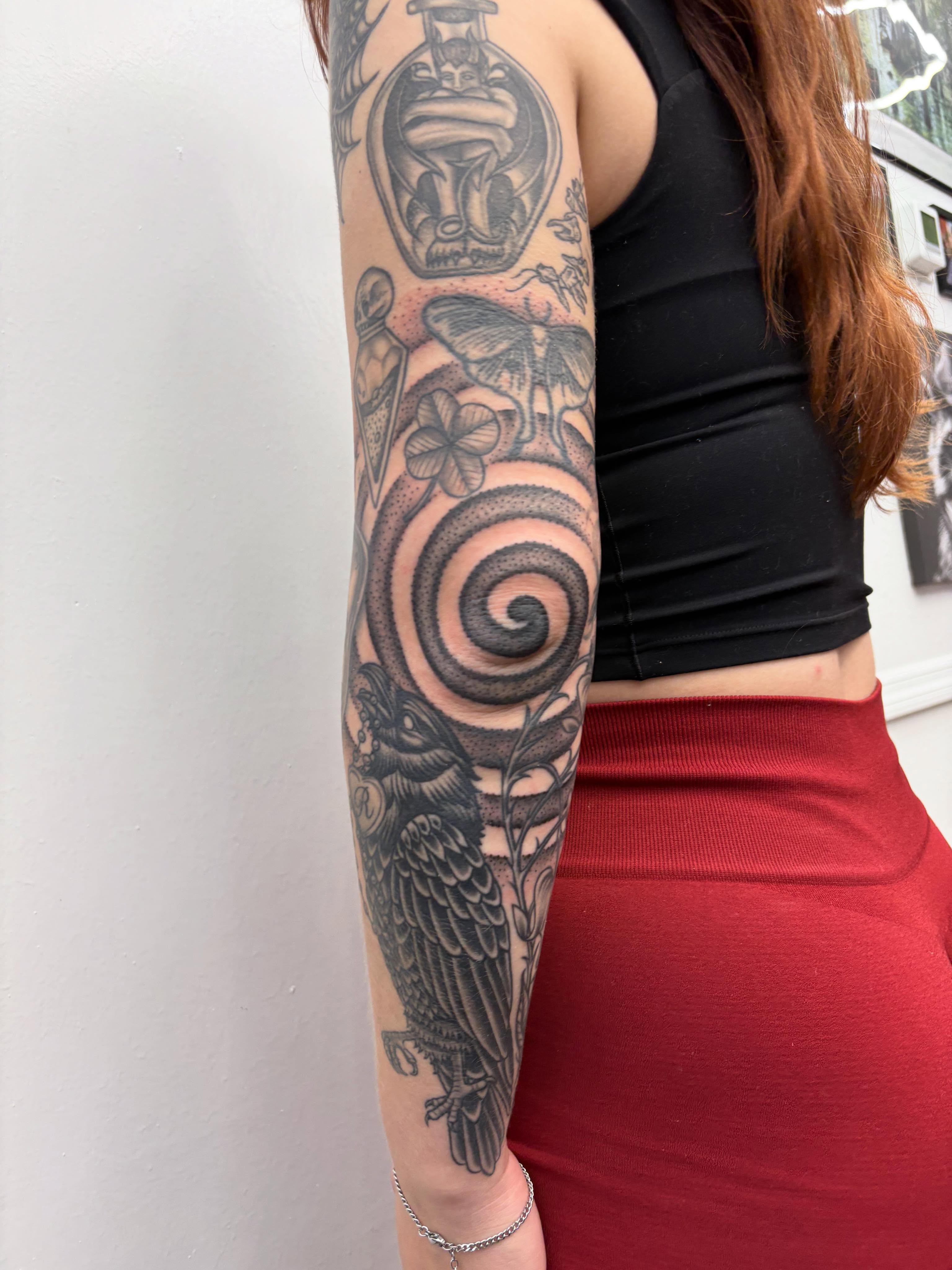 Crow and spiral black and grey tattoo on the forearm by Skye California