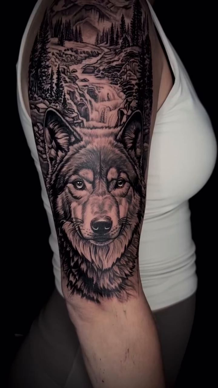Wolf with mountain and forest landscape realism tattoo on the upper arm by Joshua Orville Vaughn, Kansas City, Missouri