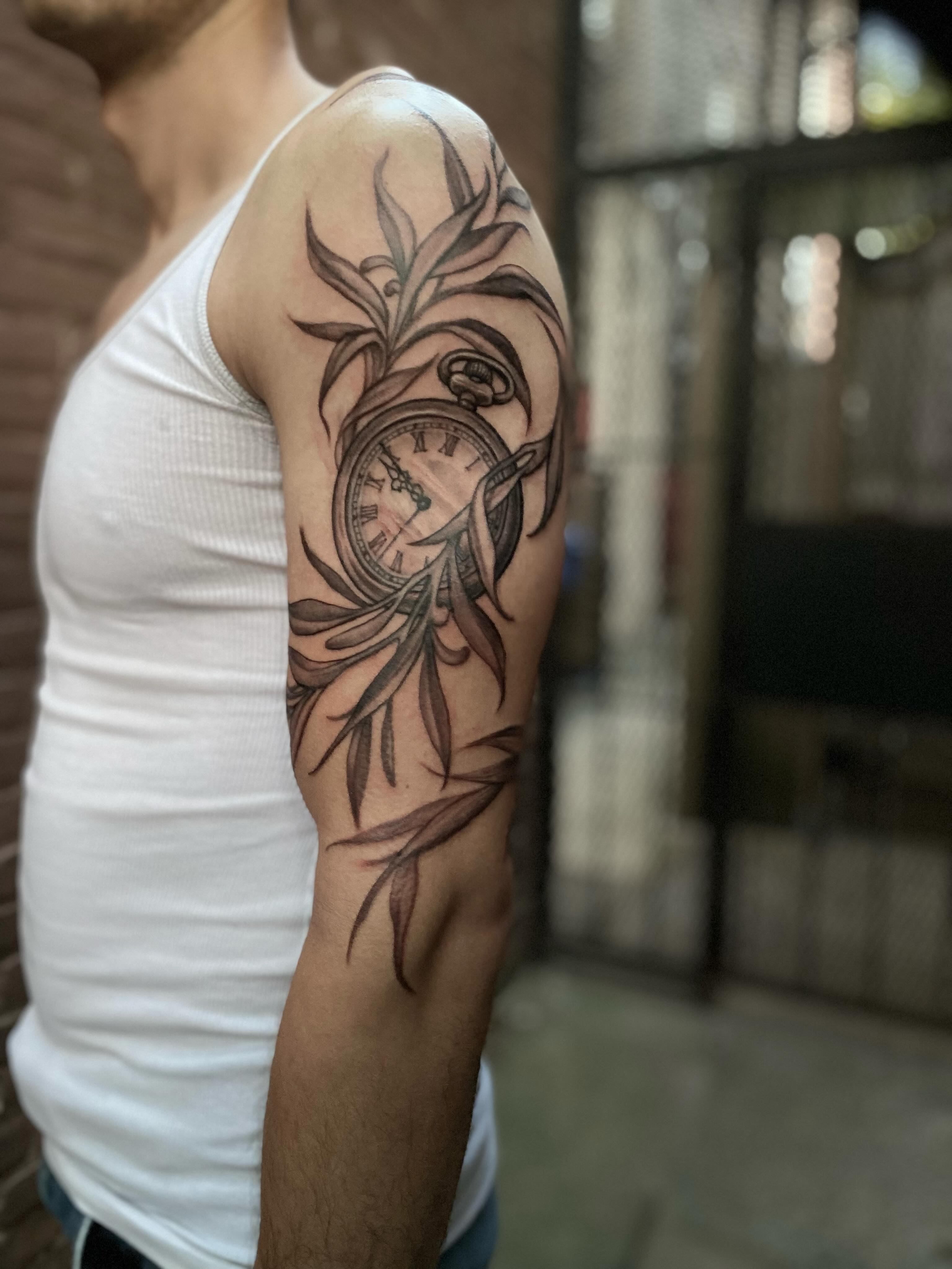 Clock and leaves black and grey tattoo on the forearm by Dana Jones