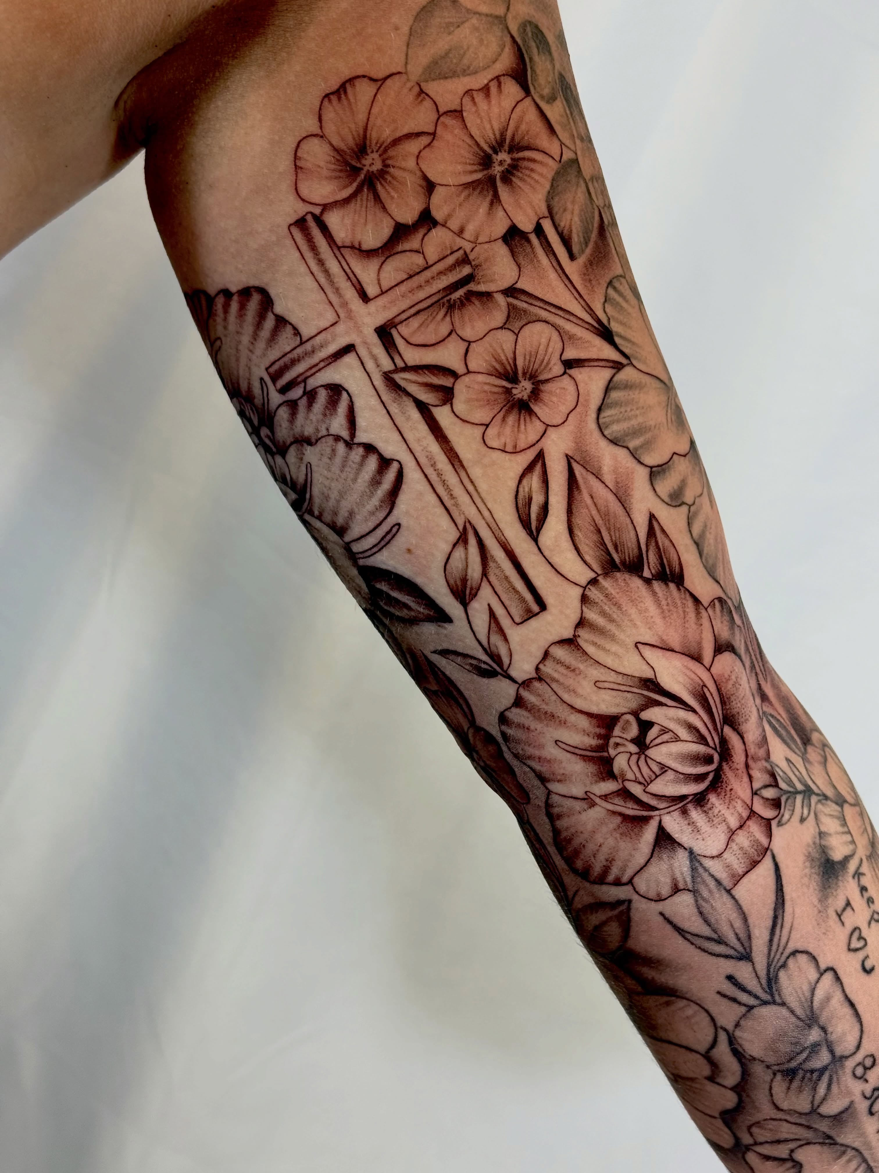 Cross and floral black and grey tattoo on the forearm by Jerry Thomas