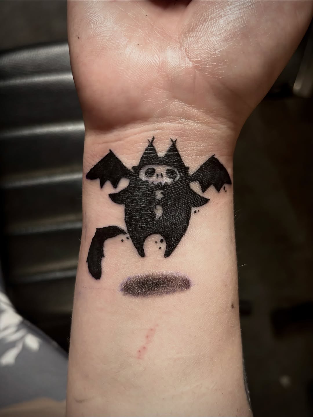Bat creature with skull face tattoo on the forearm by Rayne