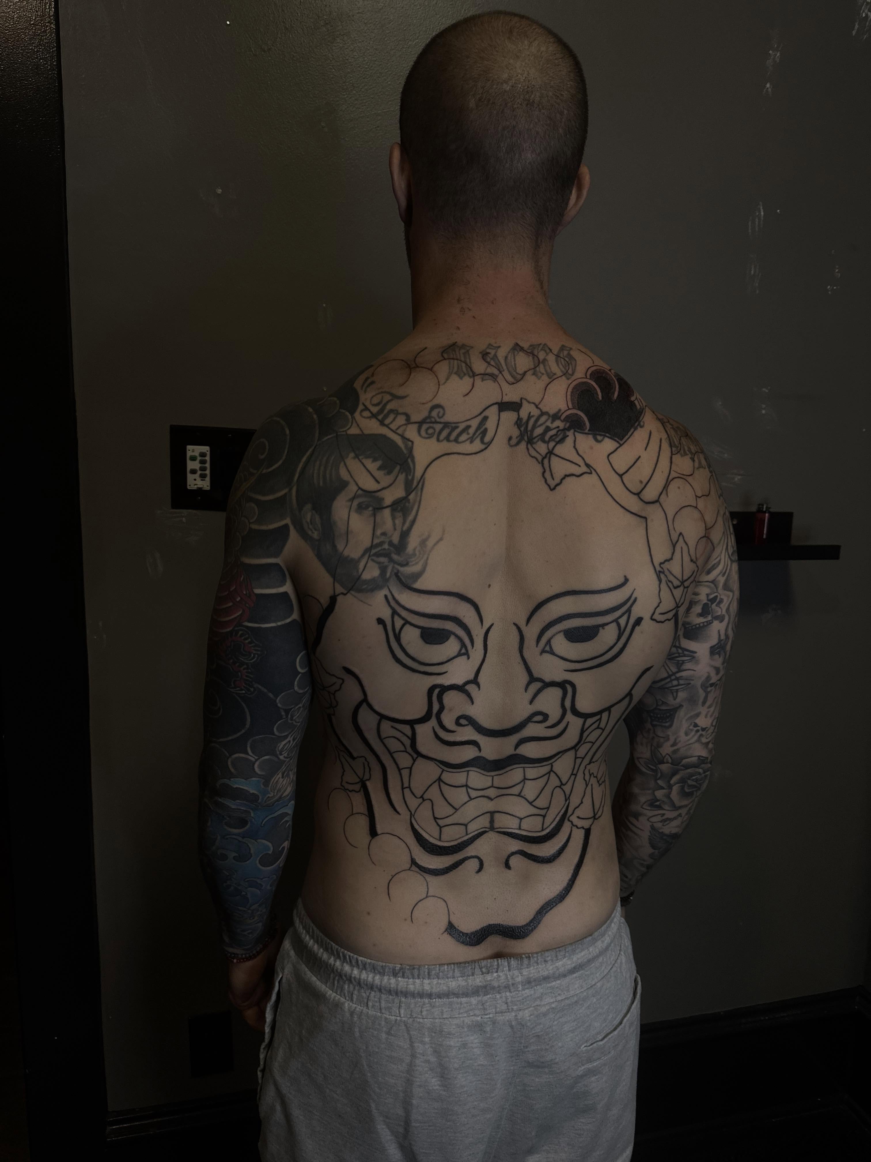 Mask black and grey tattoo on the back by Logan Perry