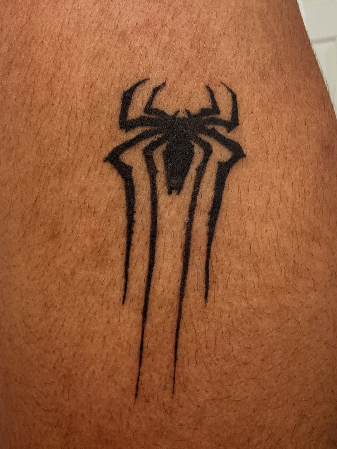 Spider logo blackwork tattoo on the thigh by winrytattoome