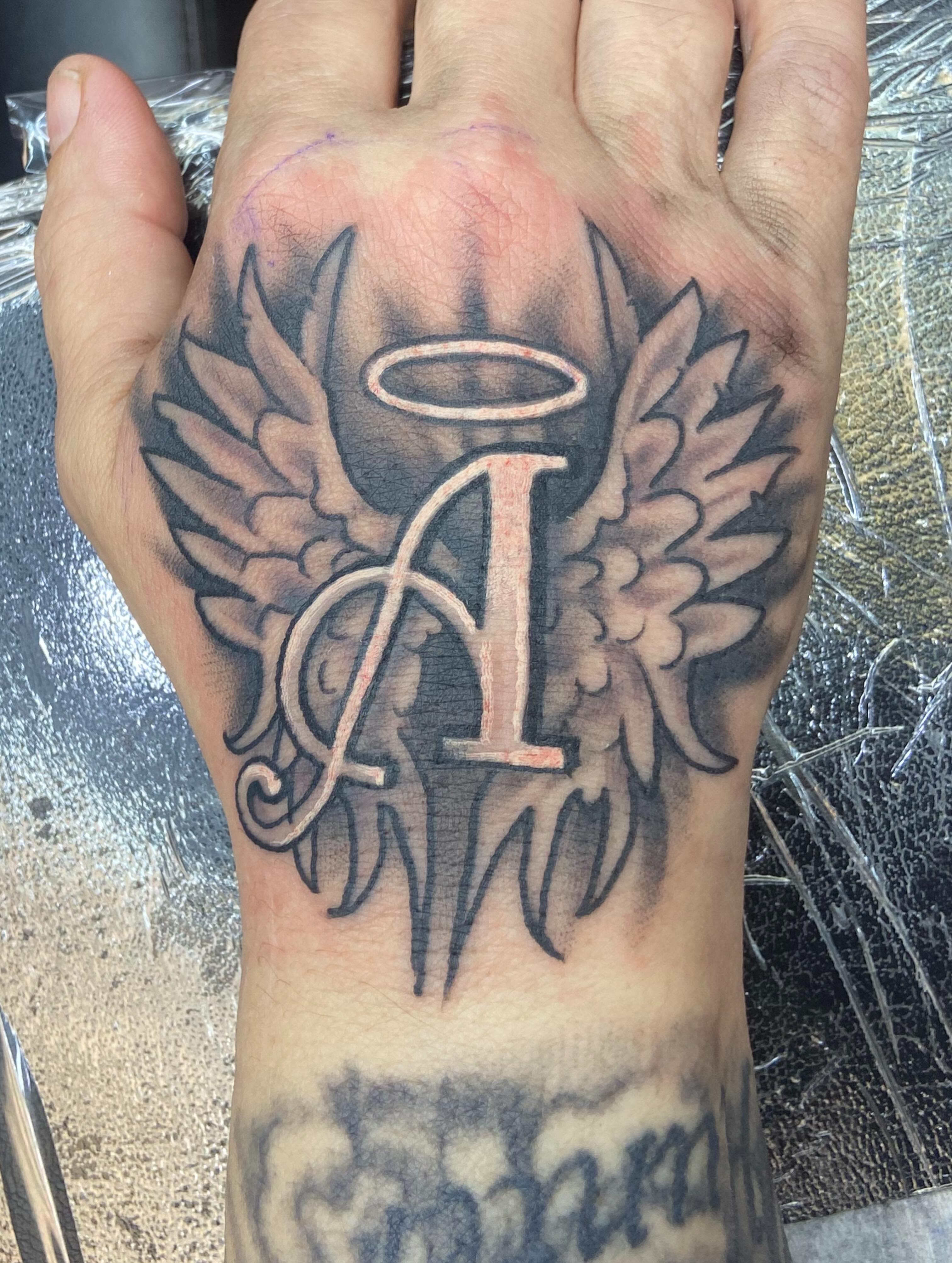 Wings and letter A black and grey tattoo on the hand by Sam Hearnen, Lawrence, Kansas