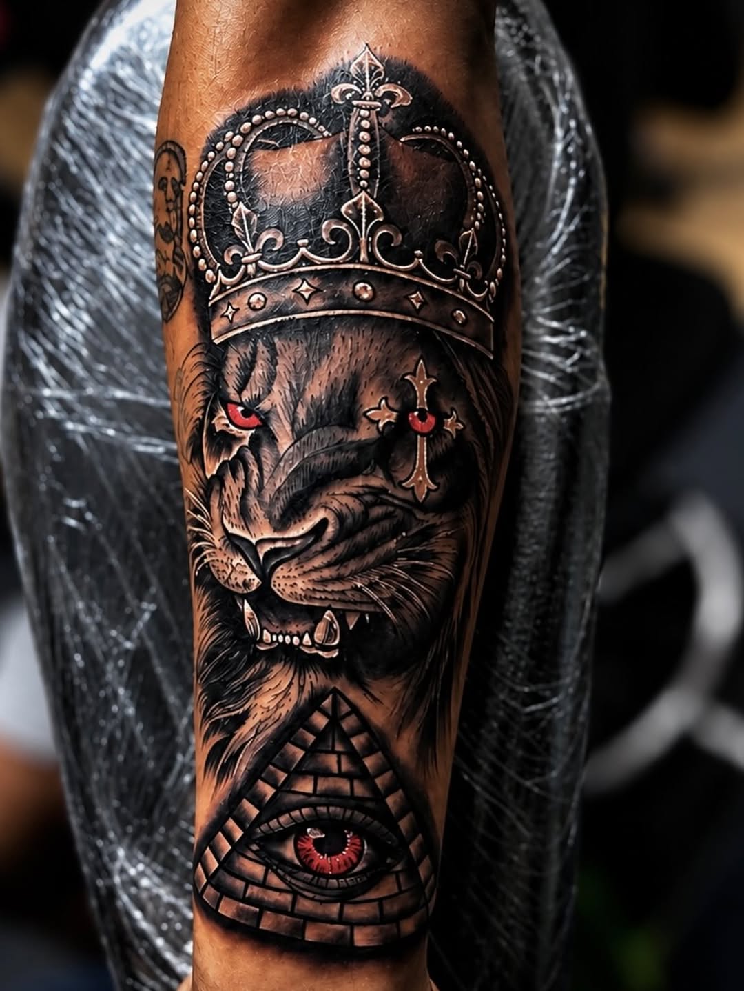 Lion with crown and eye pyramid realism tattoo on the forearm by PMU Artist