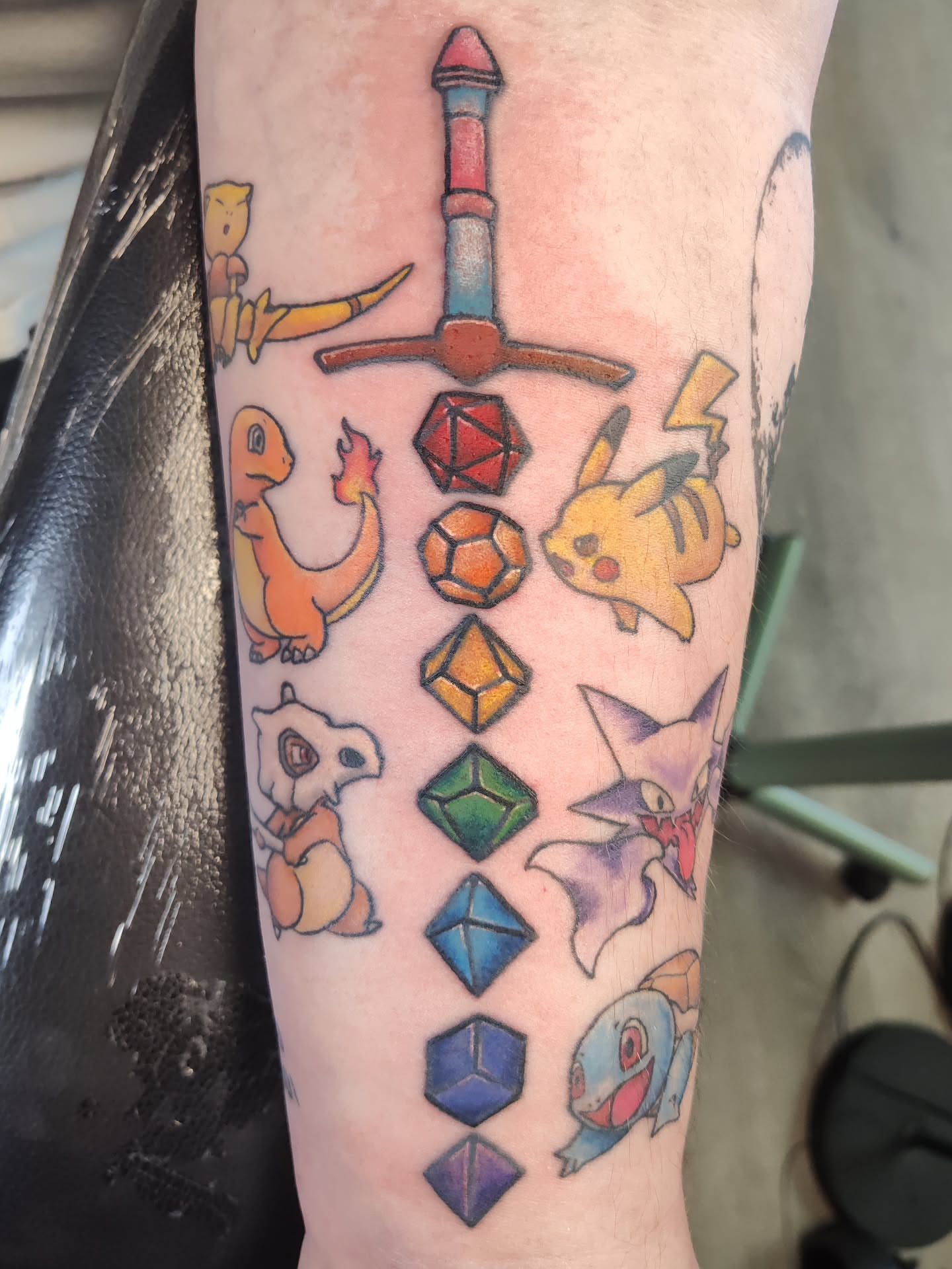 Pokémon and D&D dice geometric tattoo on the forearm by Mercury