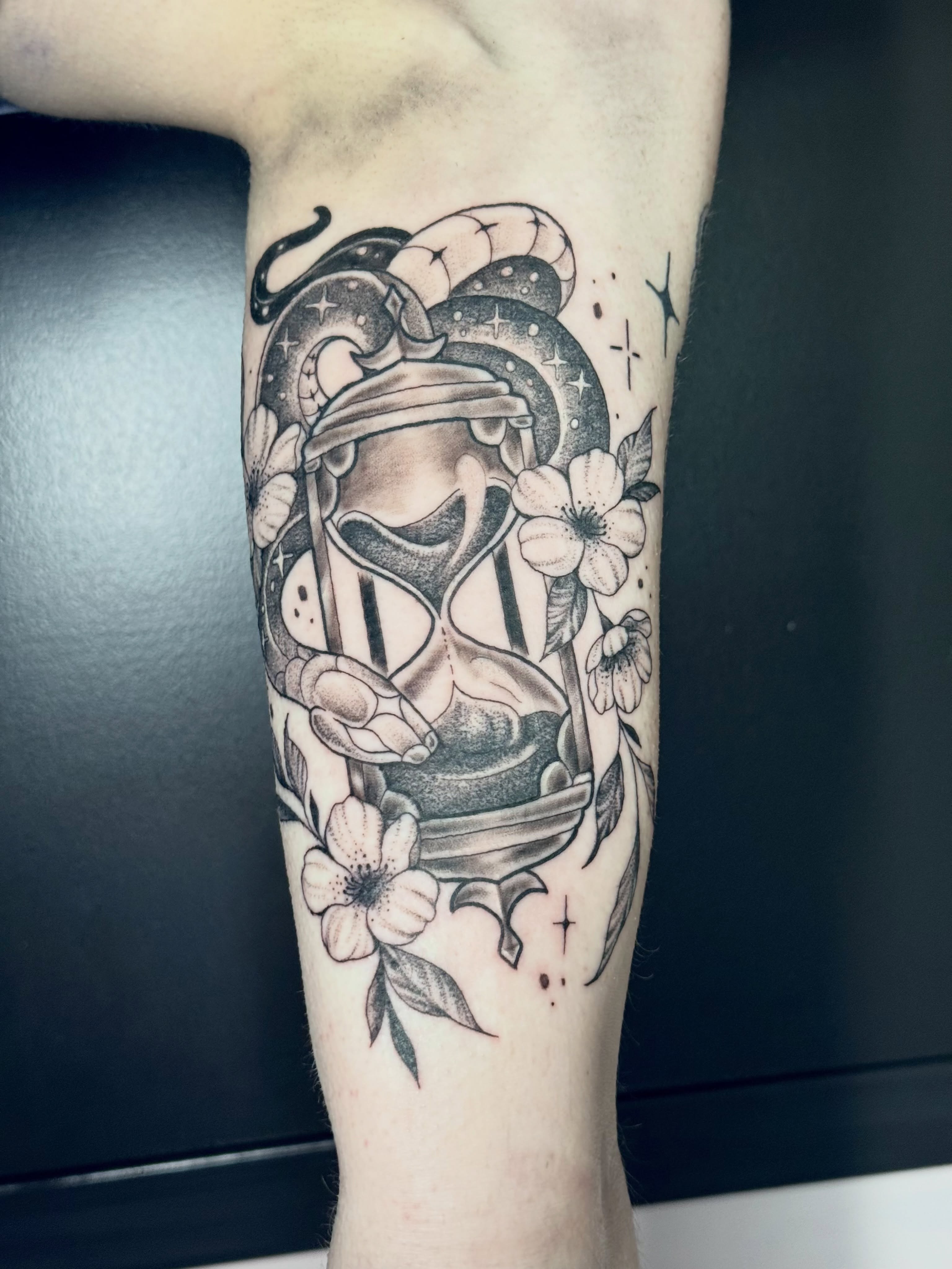 Hourglass and flowers black and grey tattoo on the forearm by Caitlynn Austin