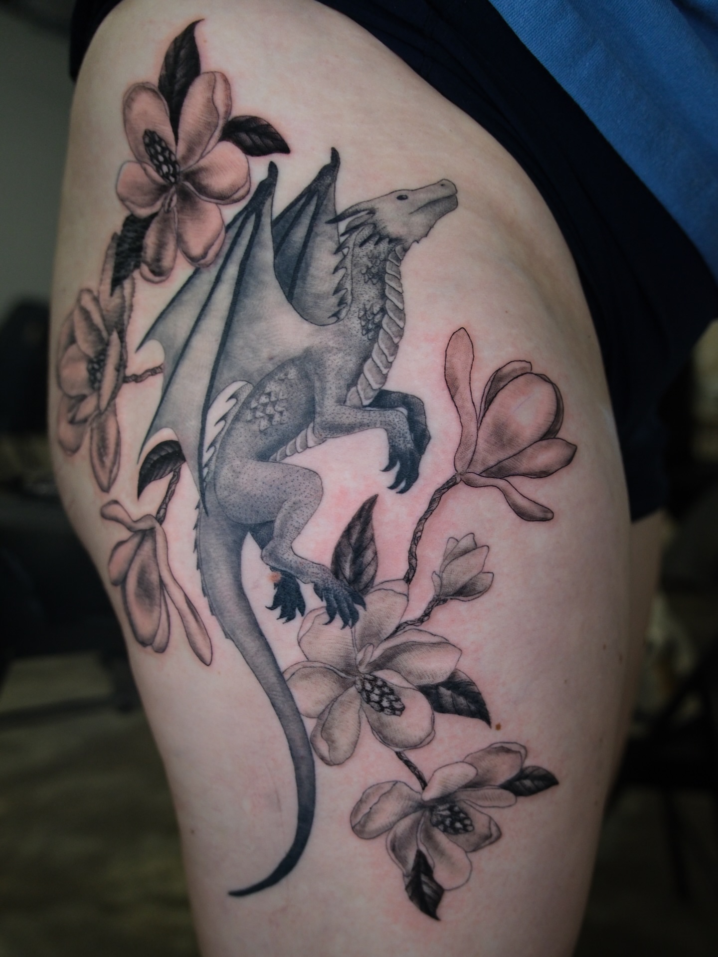 Dragon and flowers realism tattoo on the thigh by Kiana Hope
