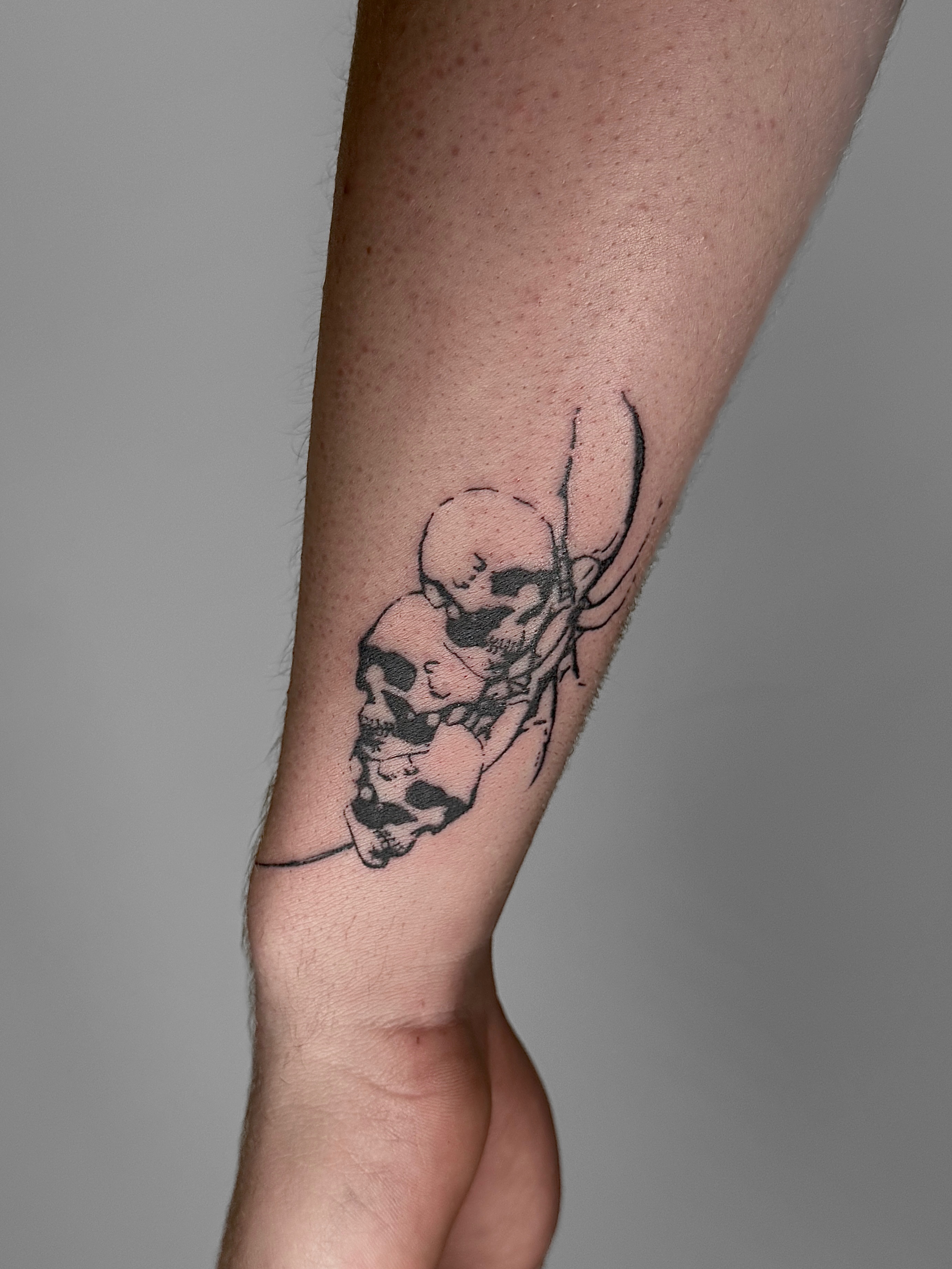 Skulls and baby black and grey tattoo on the forearm by Ava Nilou