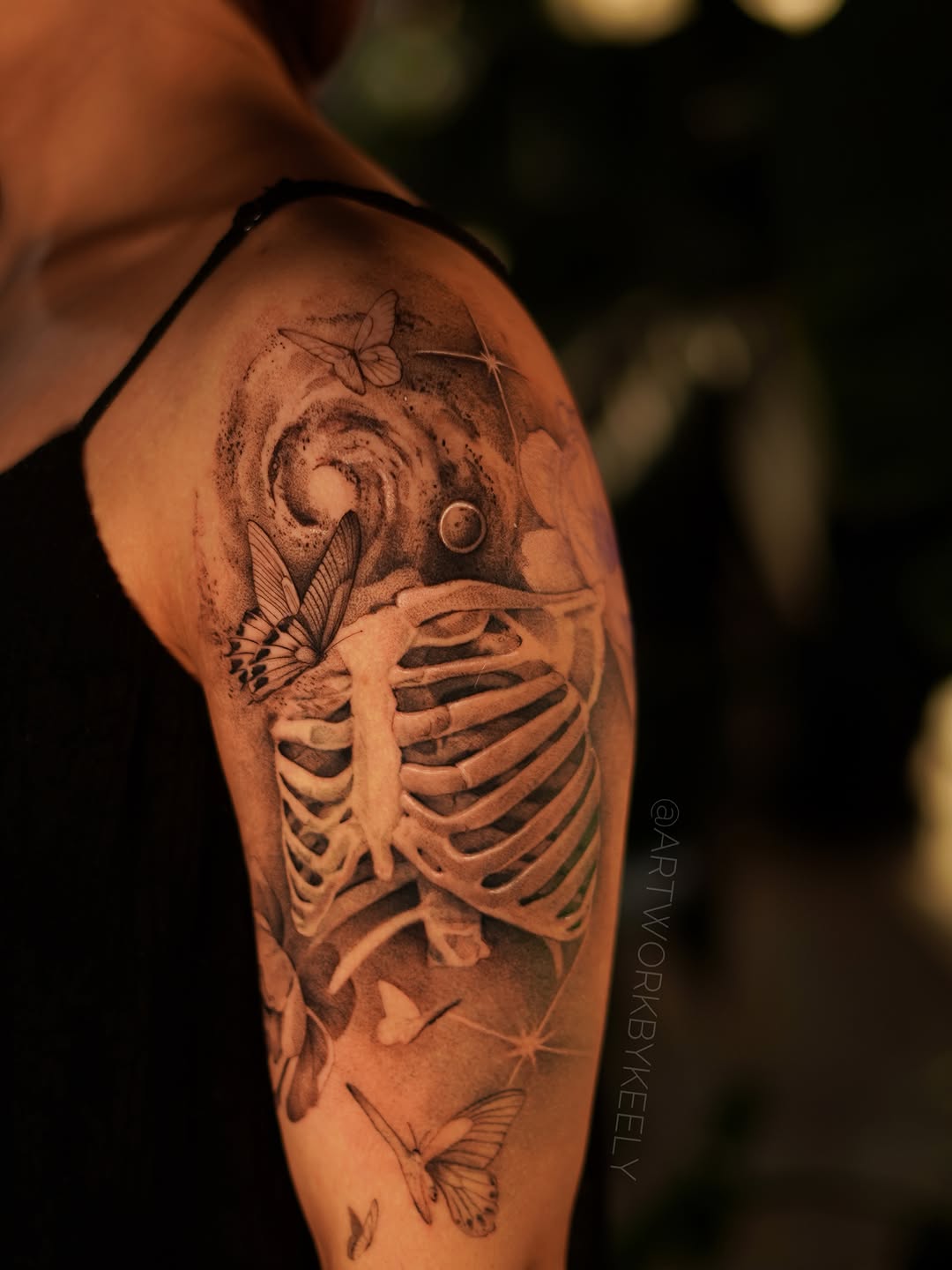 Rib cage with butterflies and galaxy surrealism tattoo on the upper arm by Keely Thompson