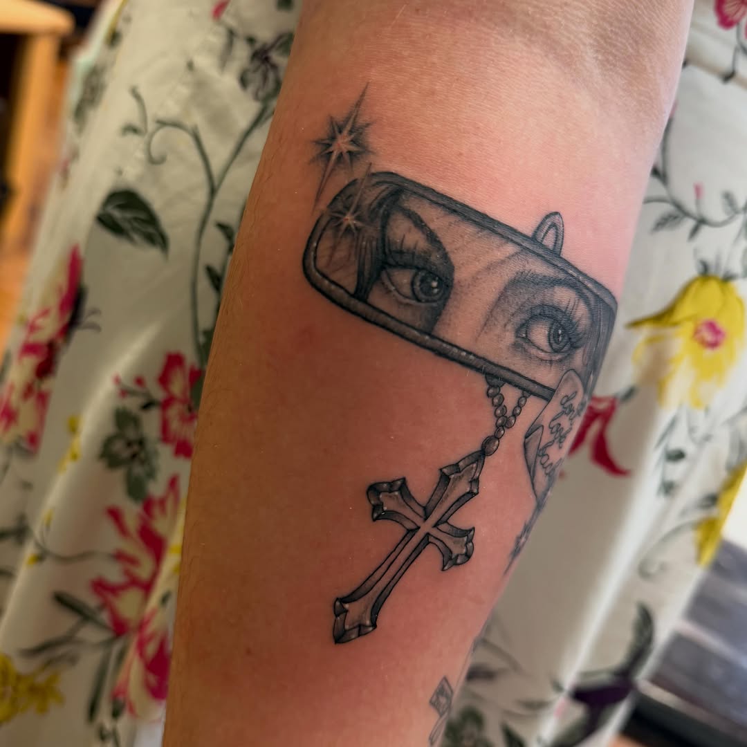 Rearview mirror with eyes and cross minimalist tattoo on the forearm by Madilynn Klassen