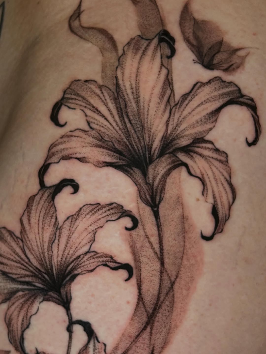 Lilies and butterfly fine line tattoo on the chest by J
