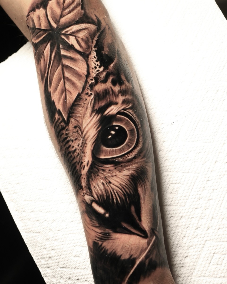 Owl face and leaf realism tattoo on the forearm by German Patiño.