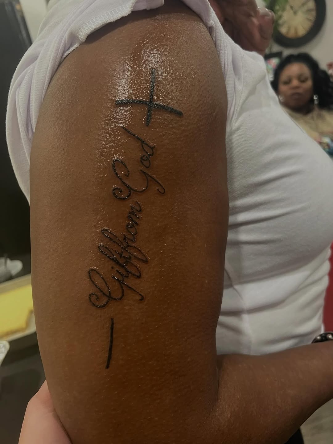 Cross and script lettering lettering tattoo on the upper arm by Tatz By Benji