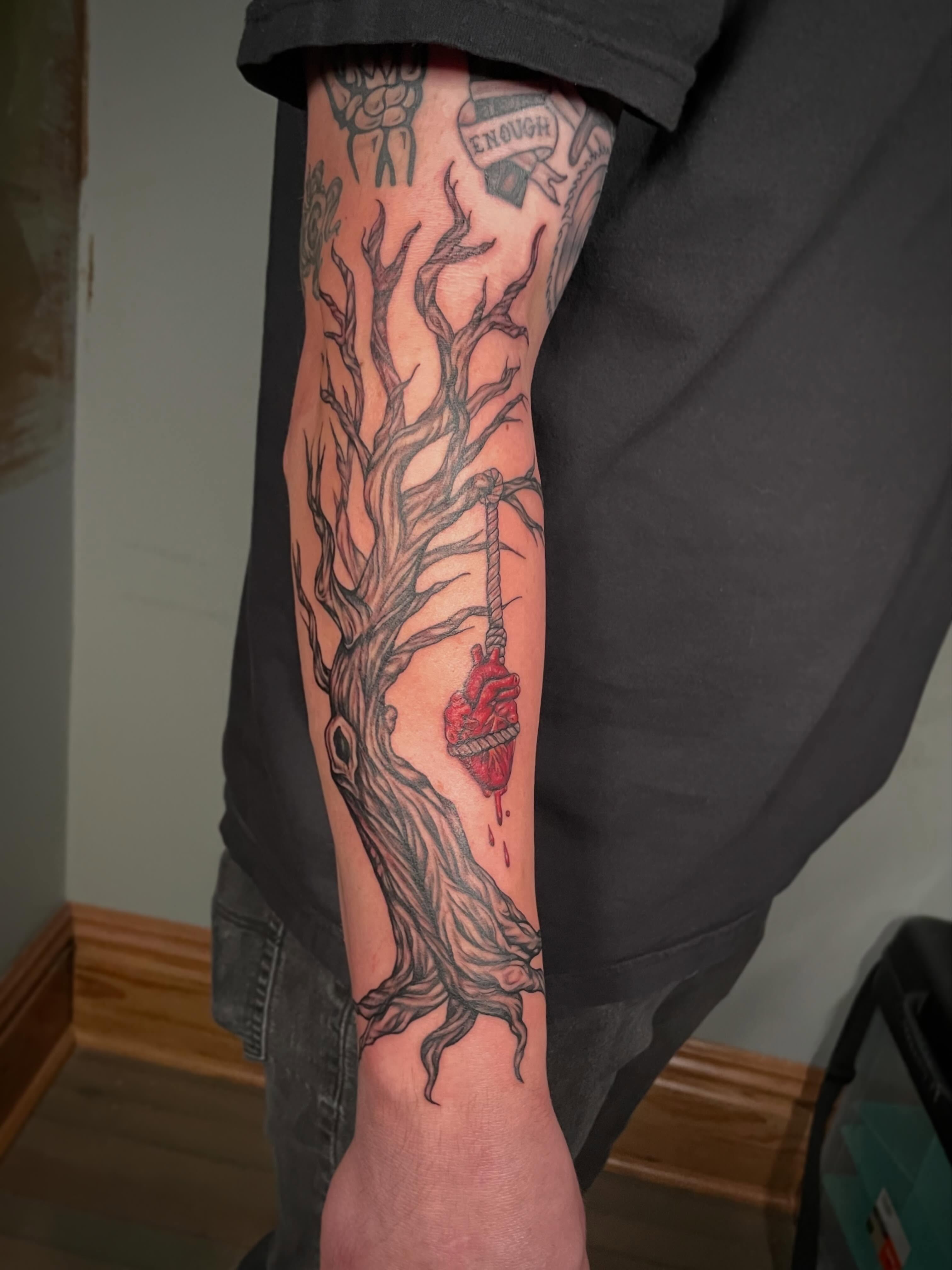 Heart hanging from tree dark realism tattoo on the forearm by Hannah Copeskey