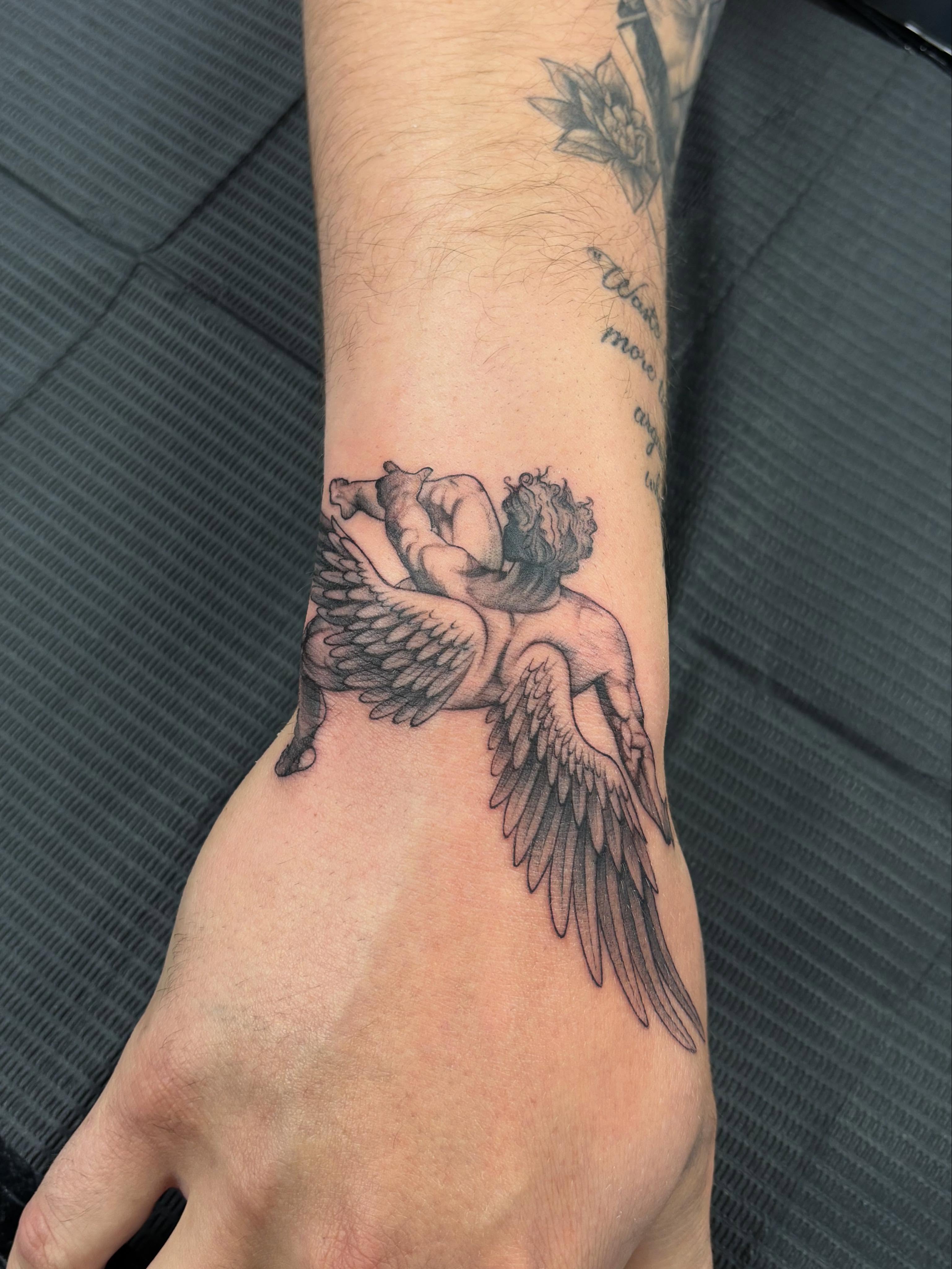 Winged cherub black and grey tattoo on the forearm by Jennifer Flores