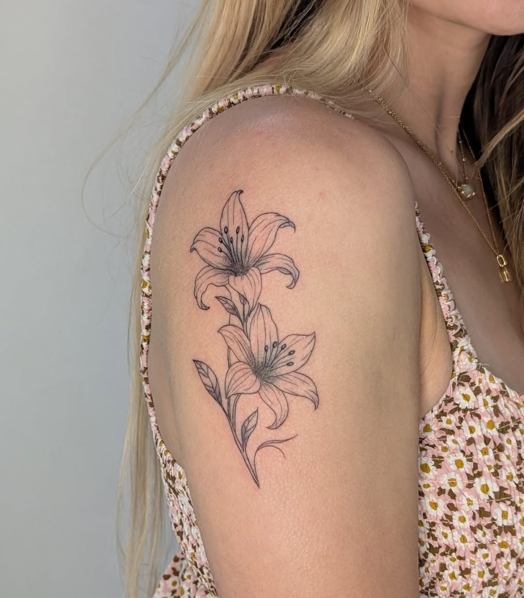 Two lilies fine line tattoo on the shoulder by Nenookaasi Martin