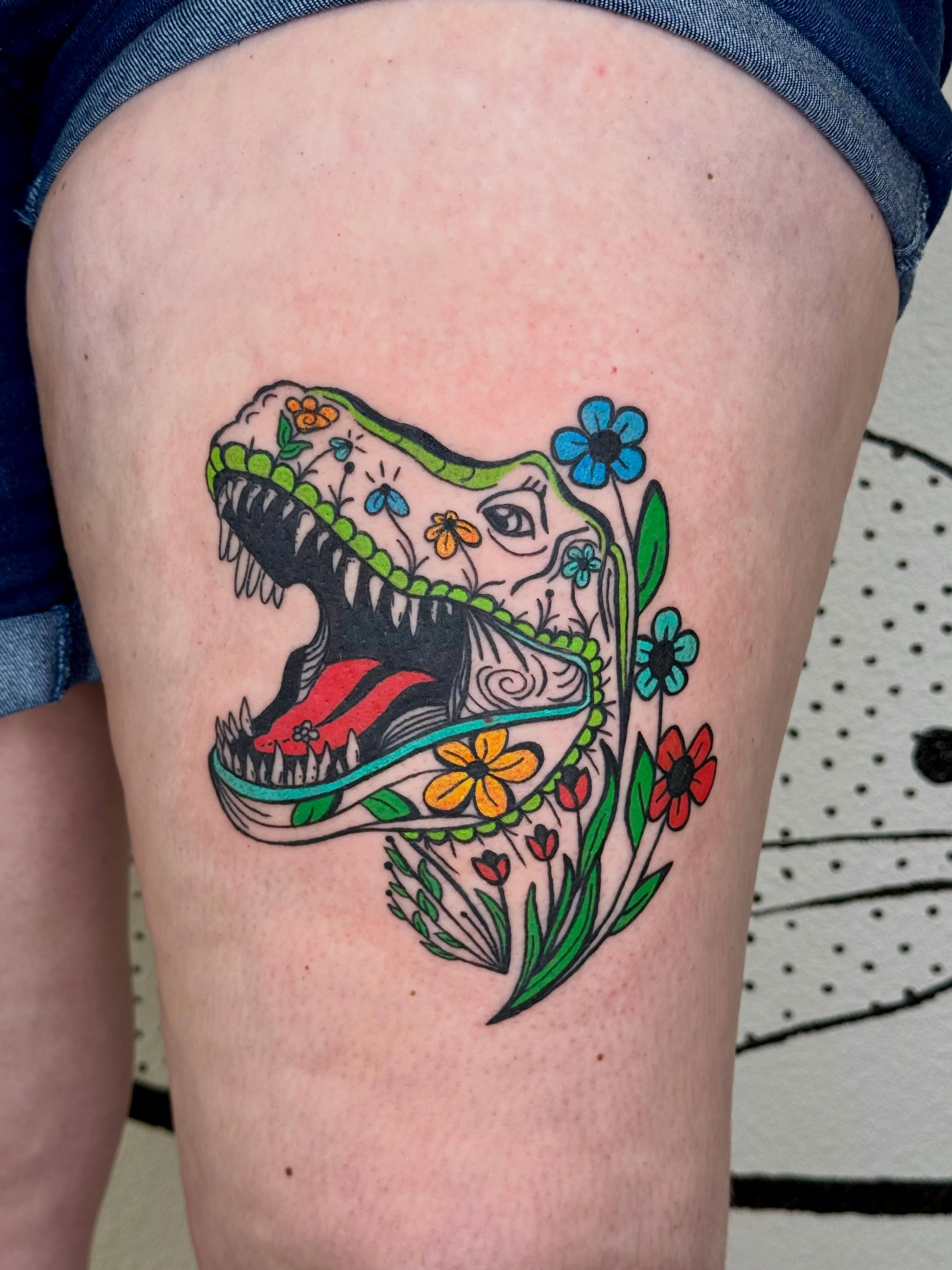 Dinosaur skull with flowers Chicano tattoo on the thigh by Peggy