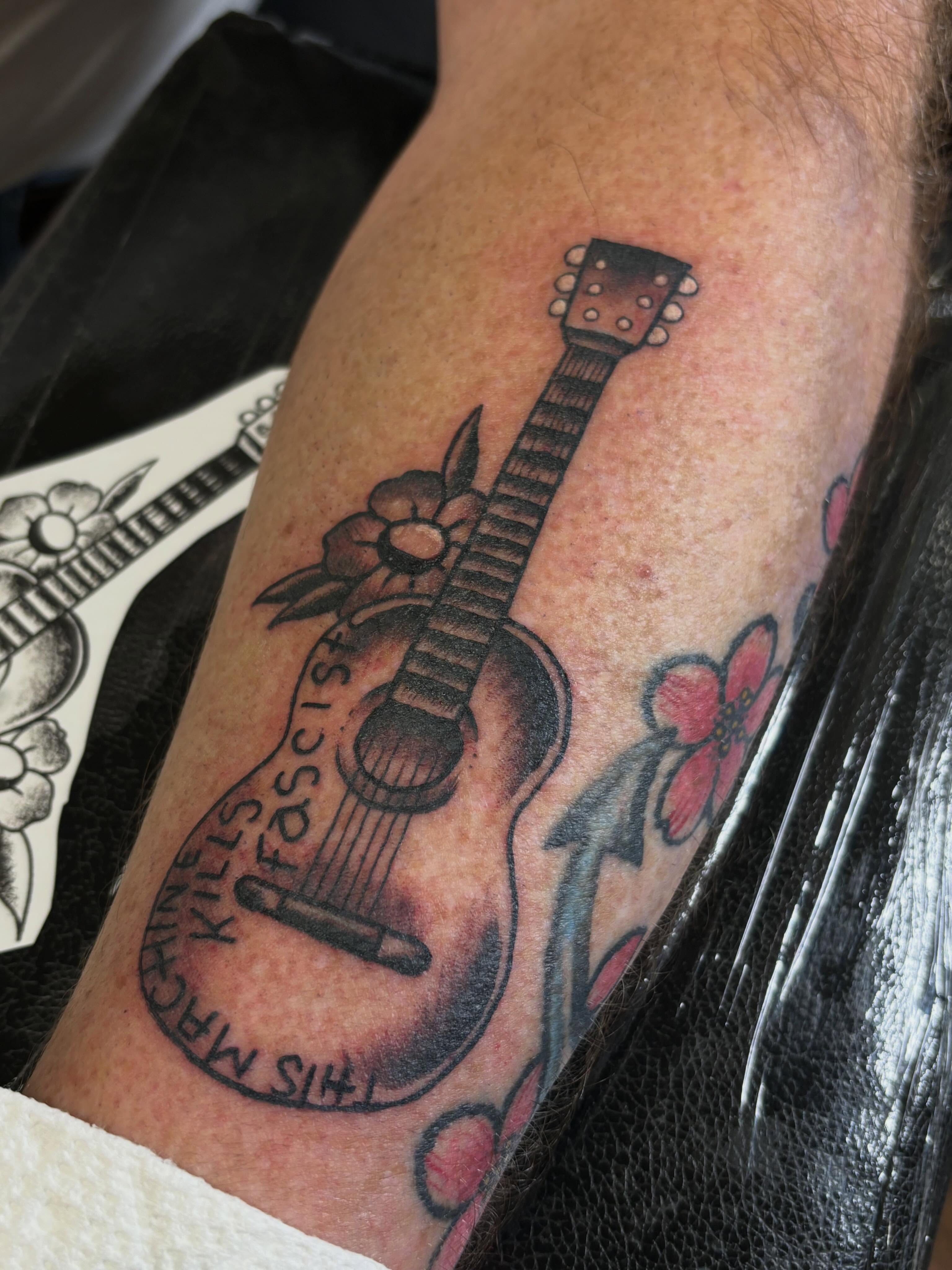 Acoustic guitar American traditional tattoo on the forearm by Nick Tate