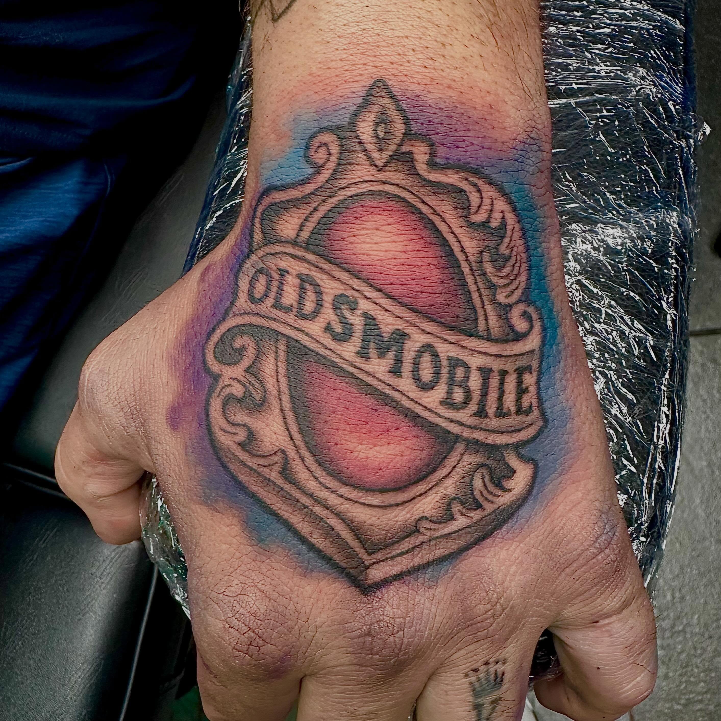 Oldsmobile shield American traditional tattoo on the hand by Mikaila Jean