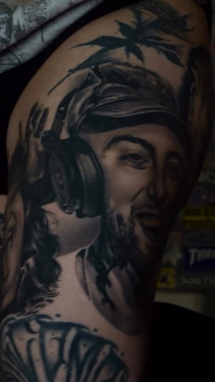 Portrait of a man with headphones Chicano tattoo on the upper arm by Dillinger, Ventura, California
