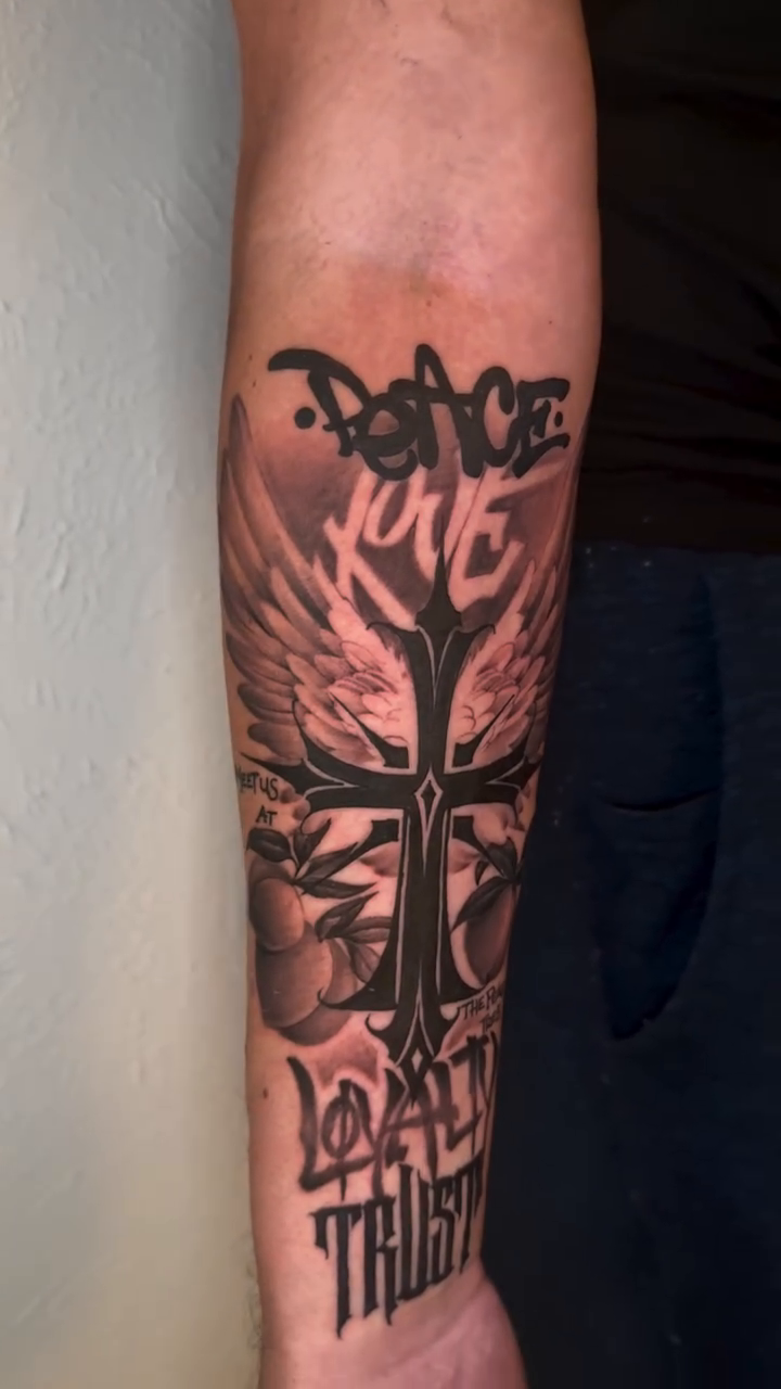 Cross with wings and lettering realism tattoo on the forearm by Mike Nance