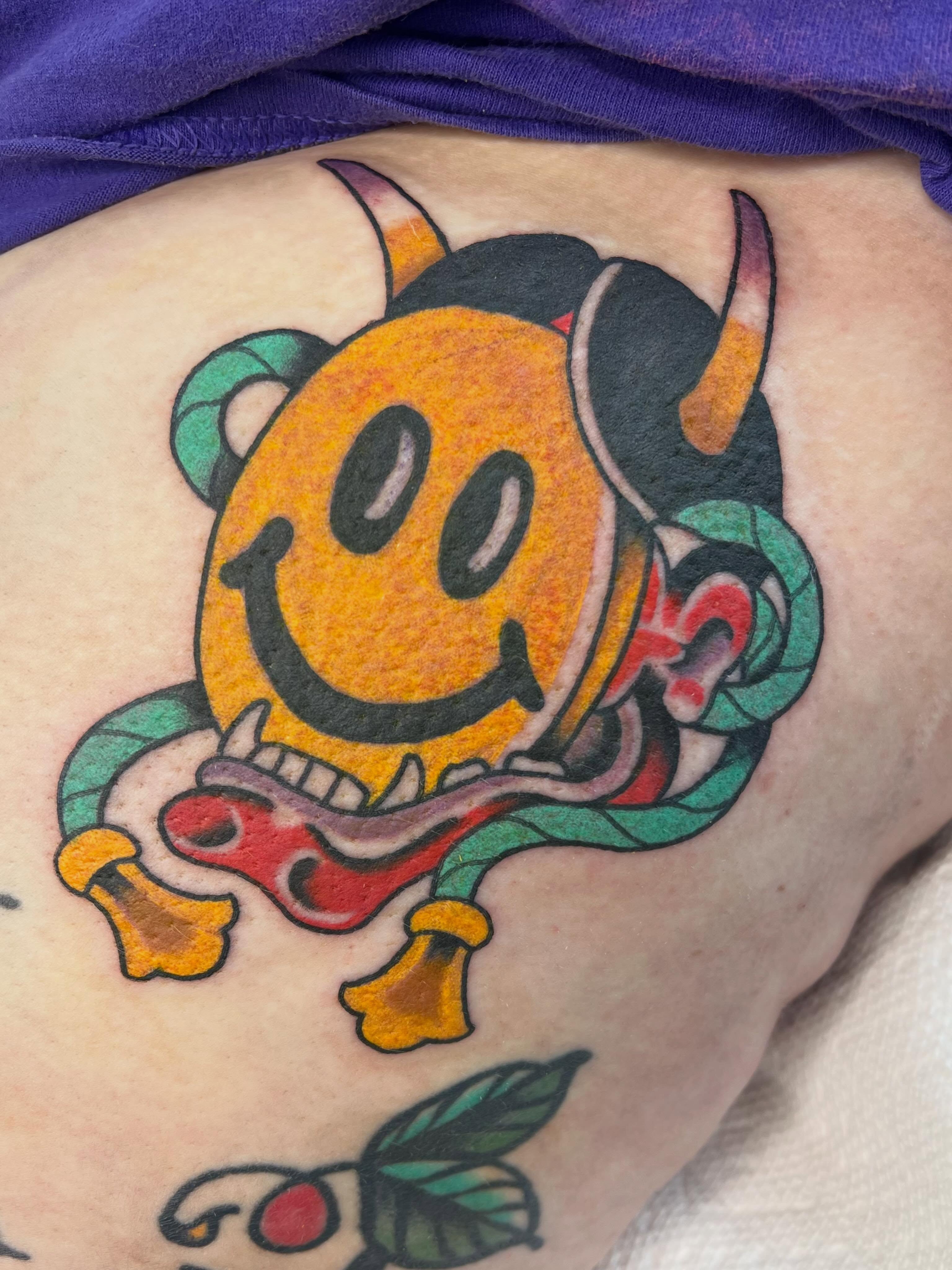 Smiley face with horns American traditional tattoo on the thigh by Brandon McDaniel Iowa Tattoo Artist