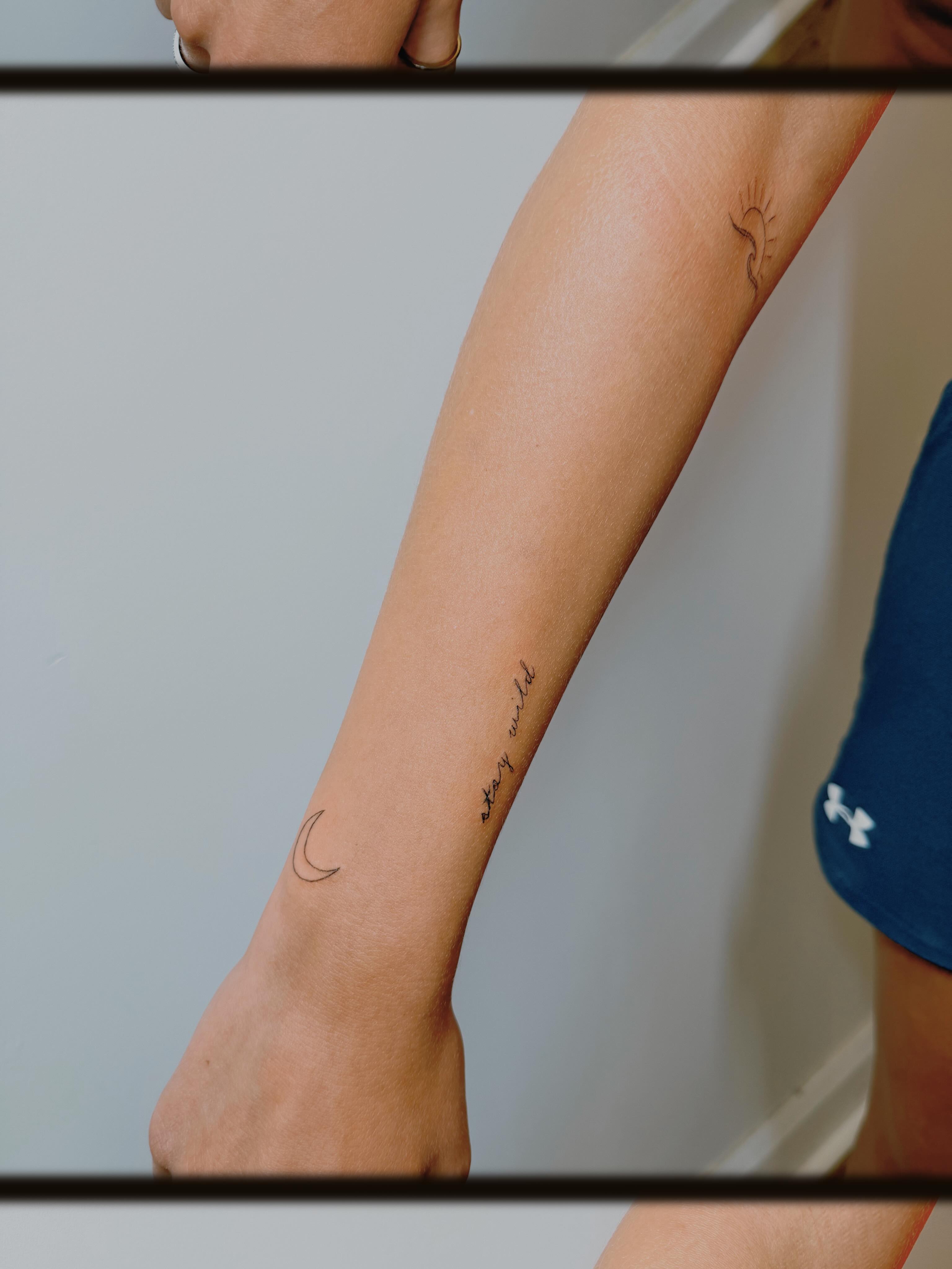 Moon and cursive text fine line tattoo on the forearm by Ashlee Burkey