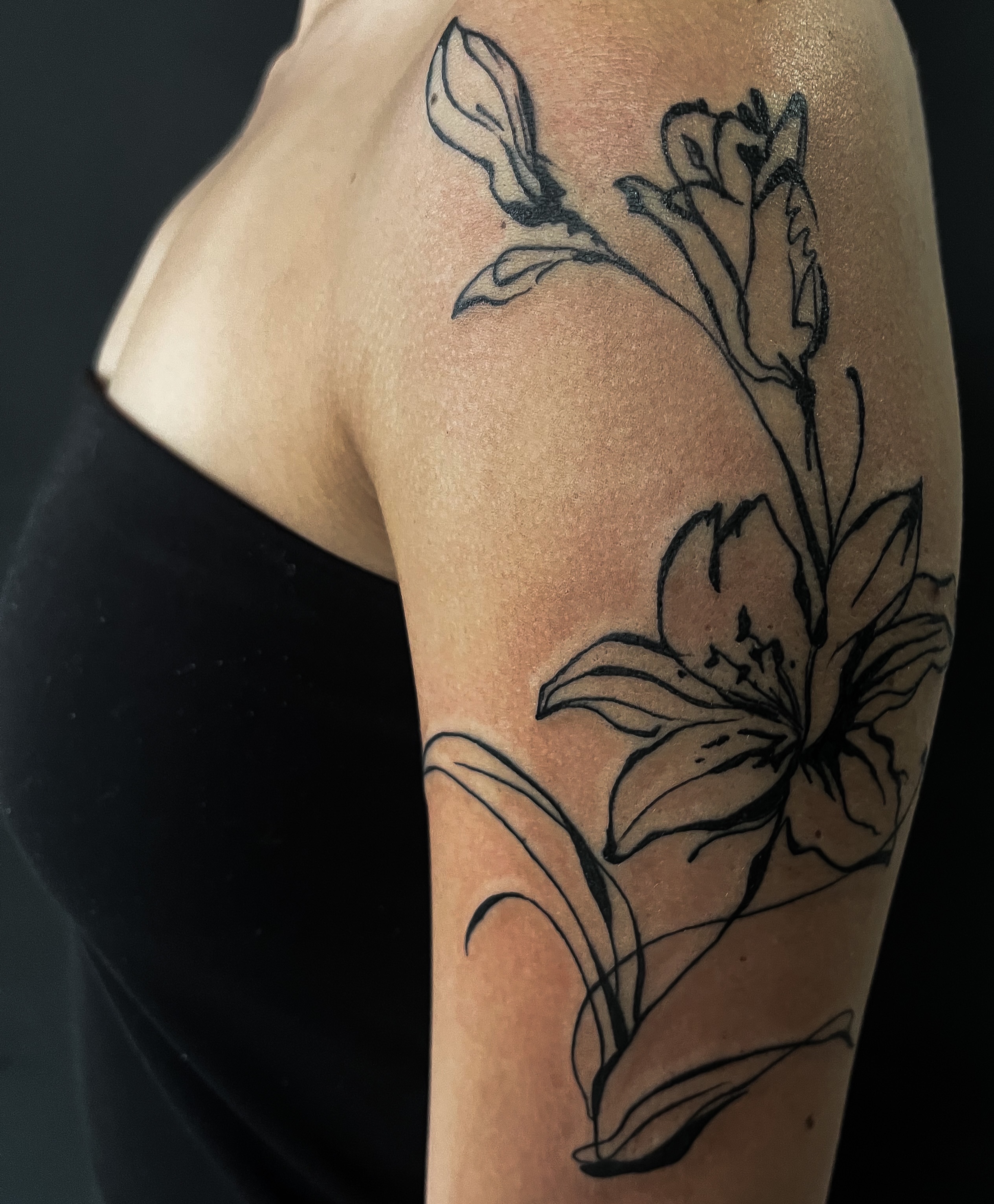 Lily black and grey tattoo on the upper arm by Janelle Cuba