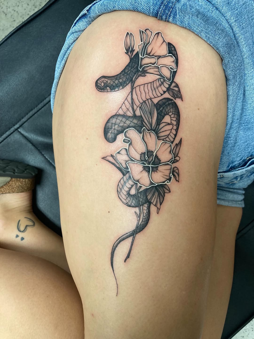 Snake and flowers fine line tattoo on the thigh by Timothy Murtaugh