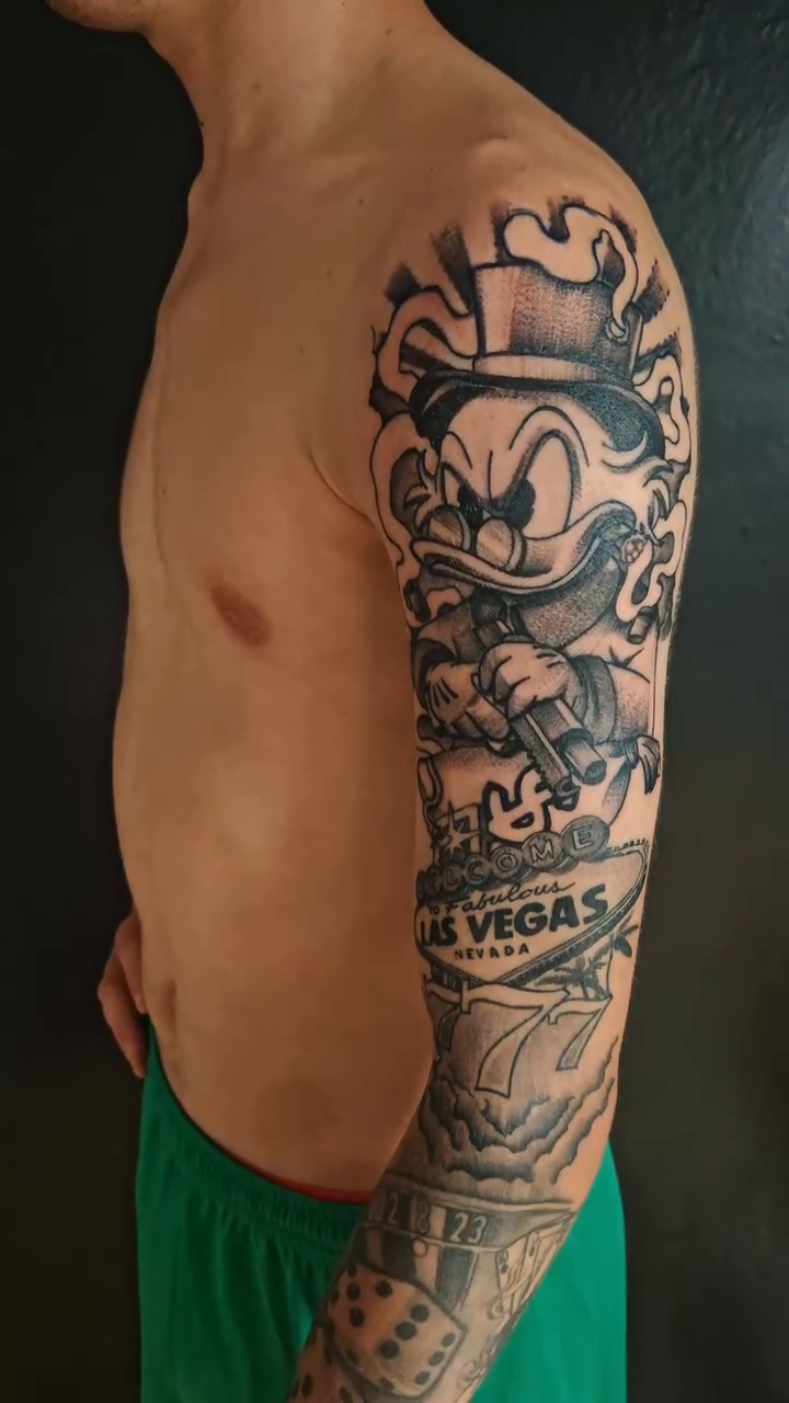 Scrooge McDuck and Vegas themed sleeve realism tattoo on the upper arm by Juanma Martin
