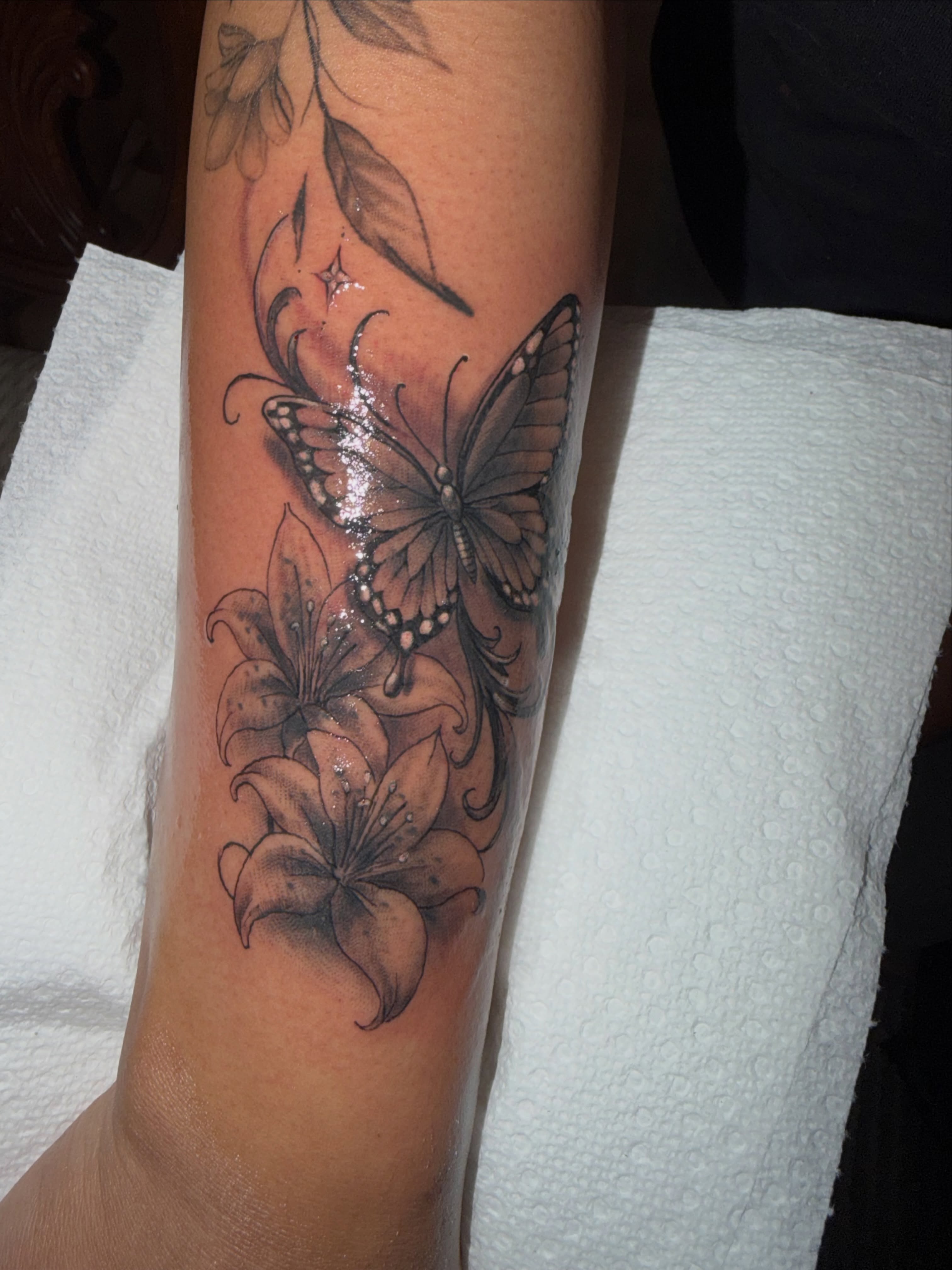 Butterfly and lilies black and grey tattoo on the forearm by Buddy K.