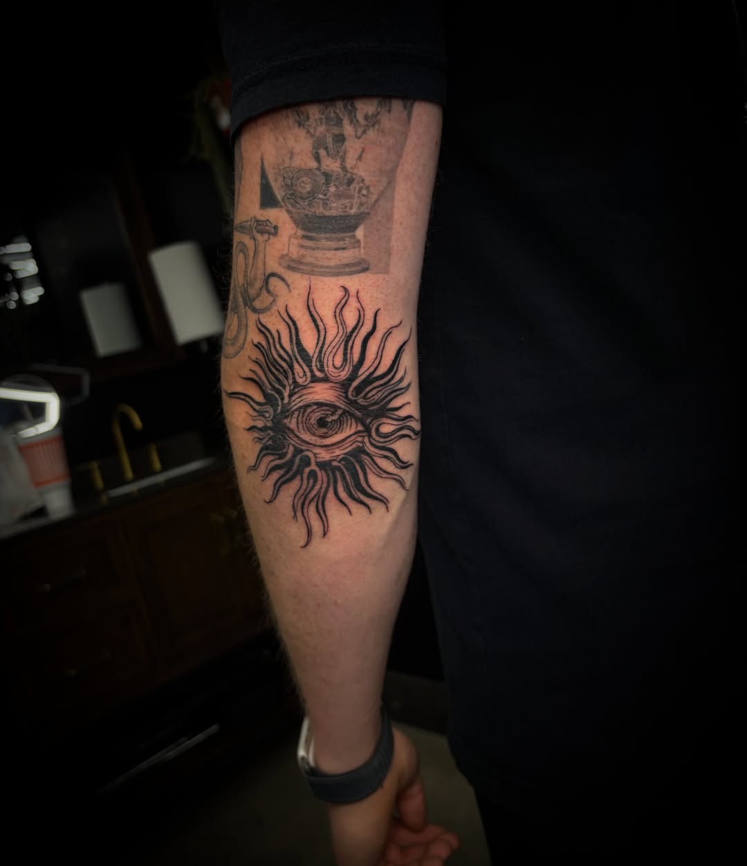Eye with sun rays black and grey tattoo on the forearm by MoogieTats