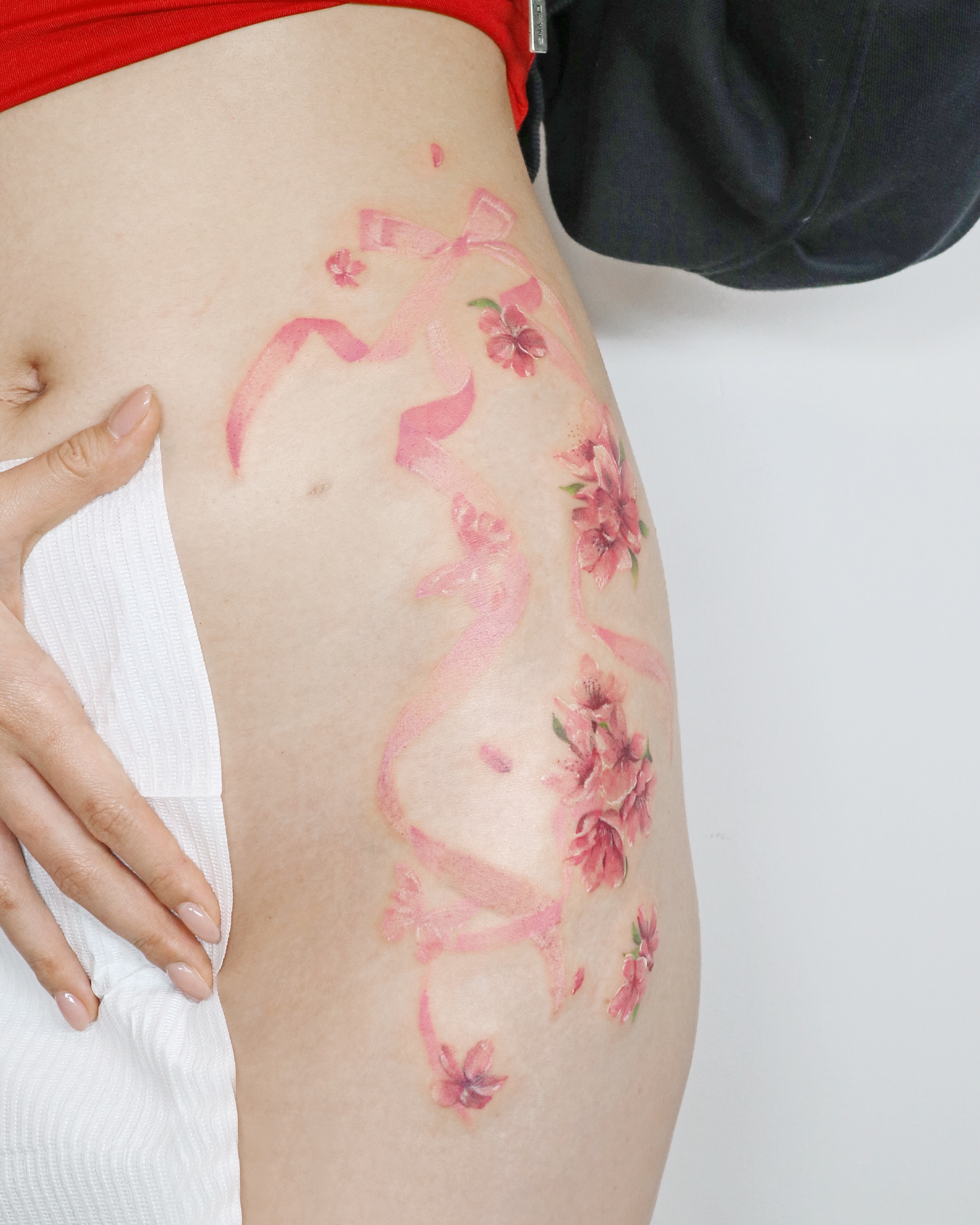 Pink ribbon and flowers watercolor tattoo on the thigh by Aroha