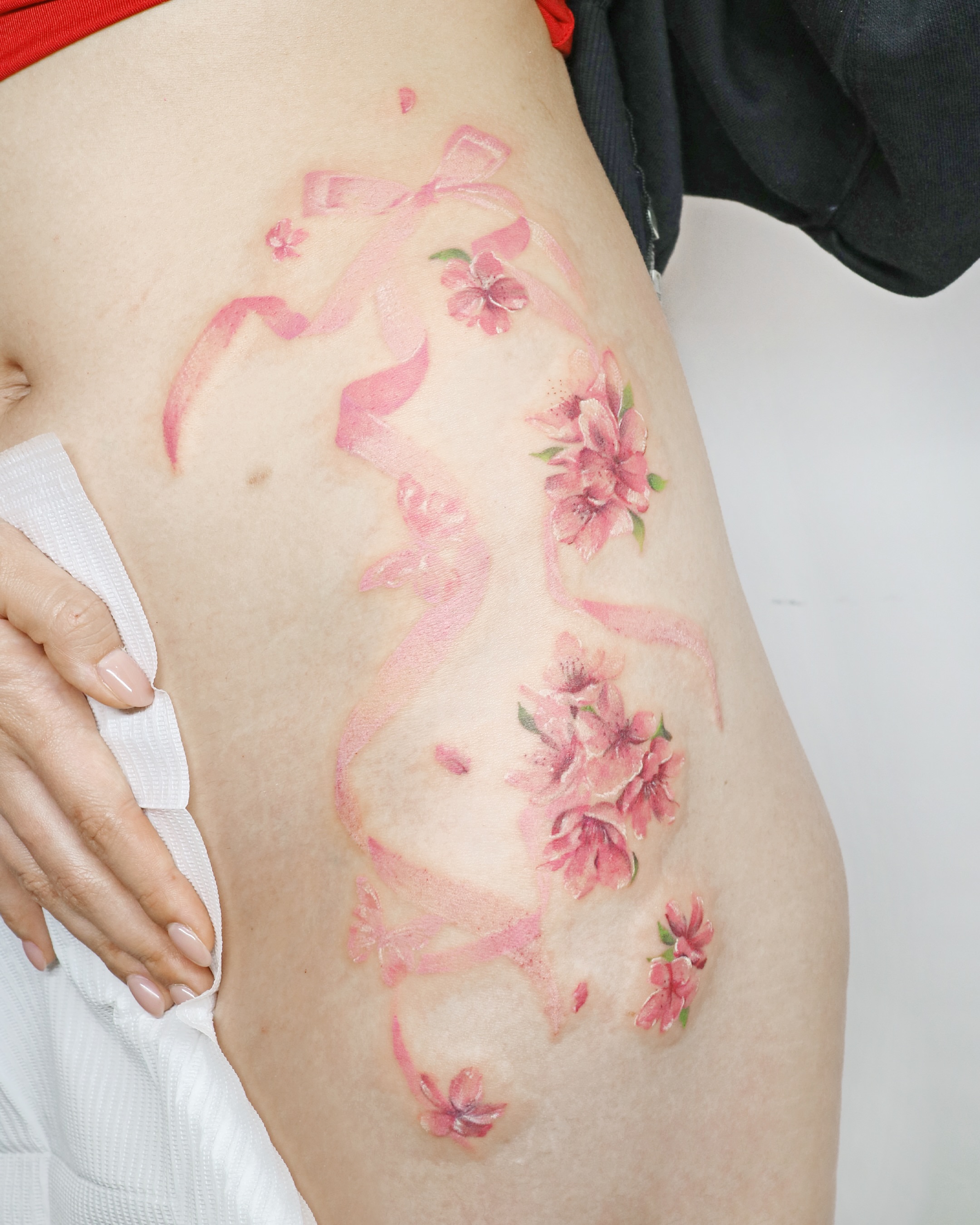 Cherry blossoms and ribbon realism tattoo on the thigh by Aroha