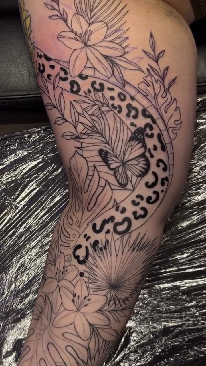 Leopard print and tropical foliage realism tattoo on the leg by Pretty Ugly Tattoos