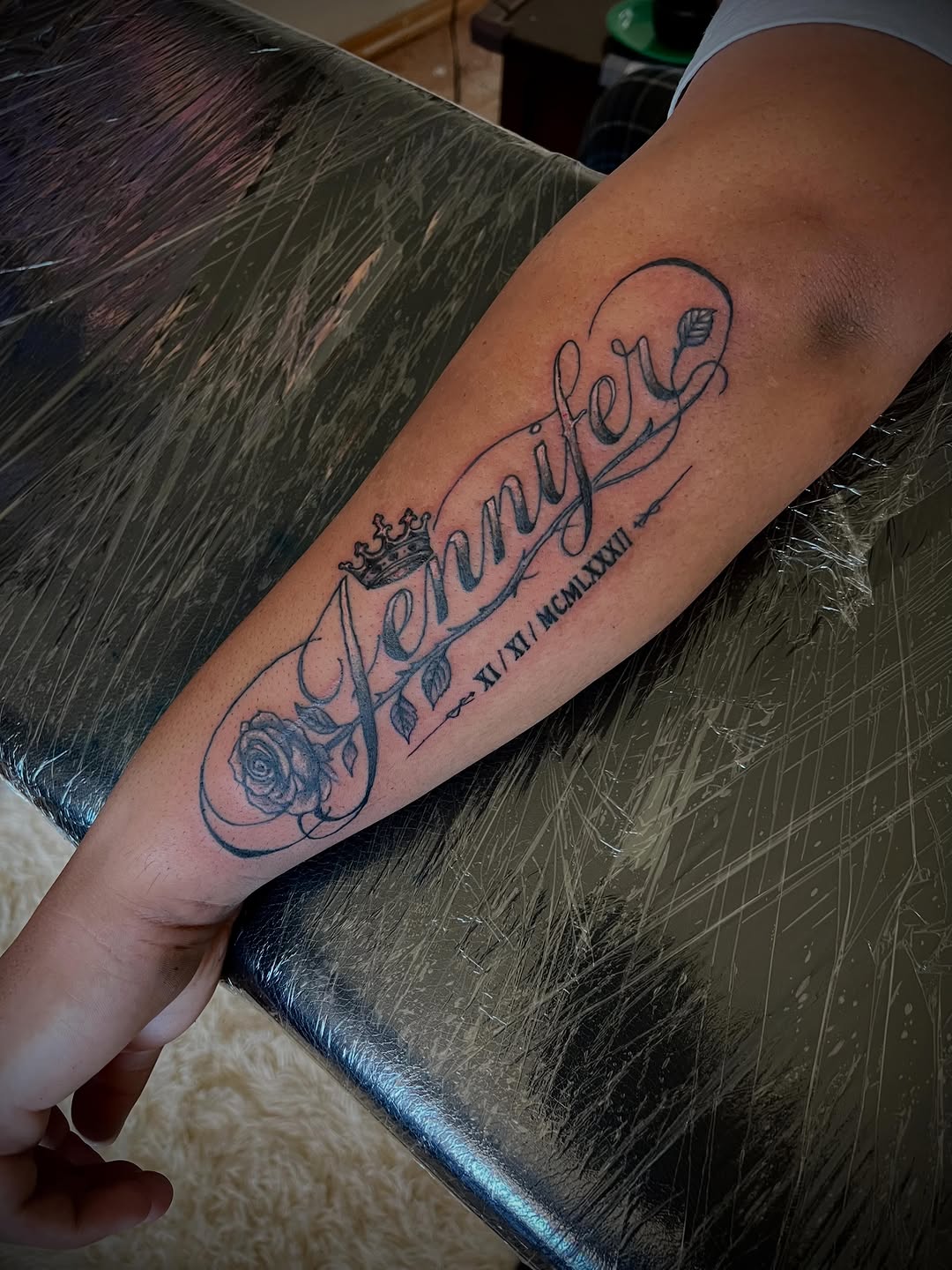 Name Jennifer with rose and crown lettering tattoo on the forearm by Jelani