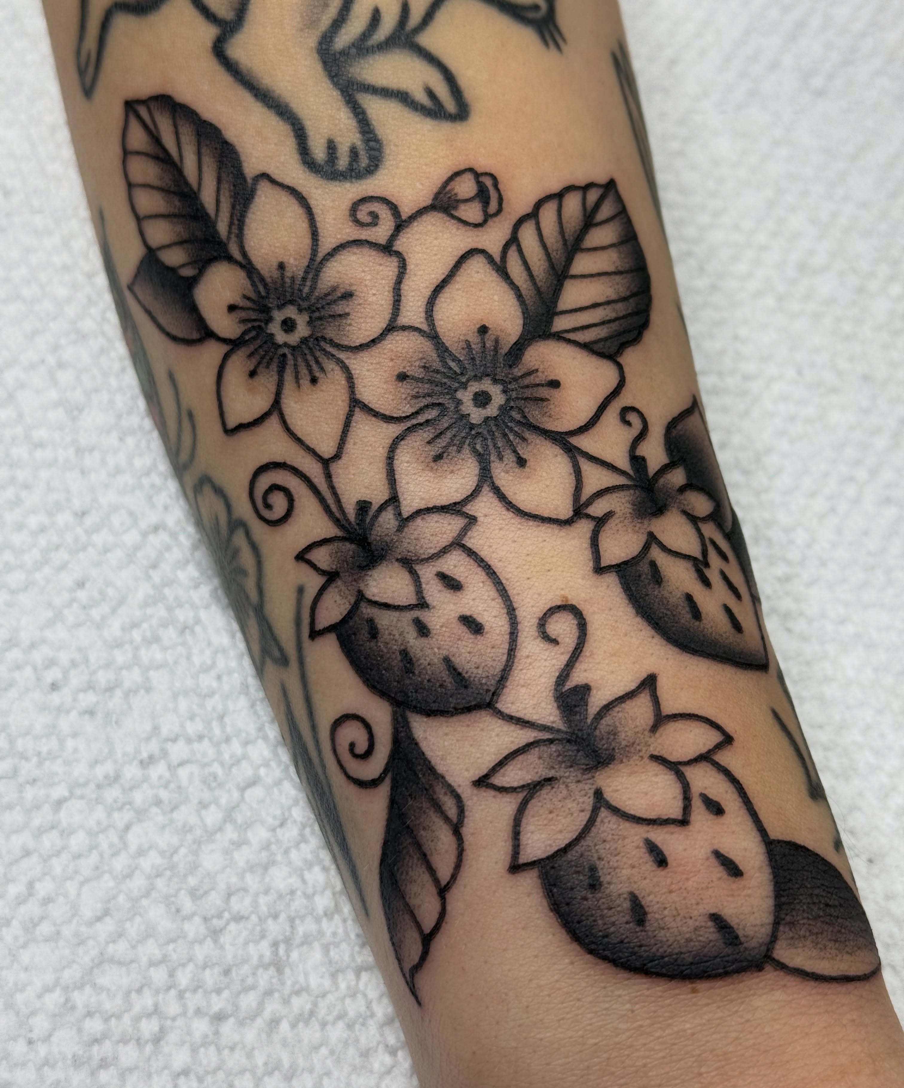 Strawberries and flowers black and grey tattoo on the forearm by Kara Mosqueda
