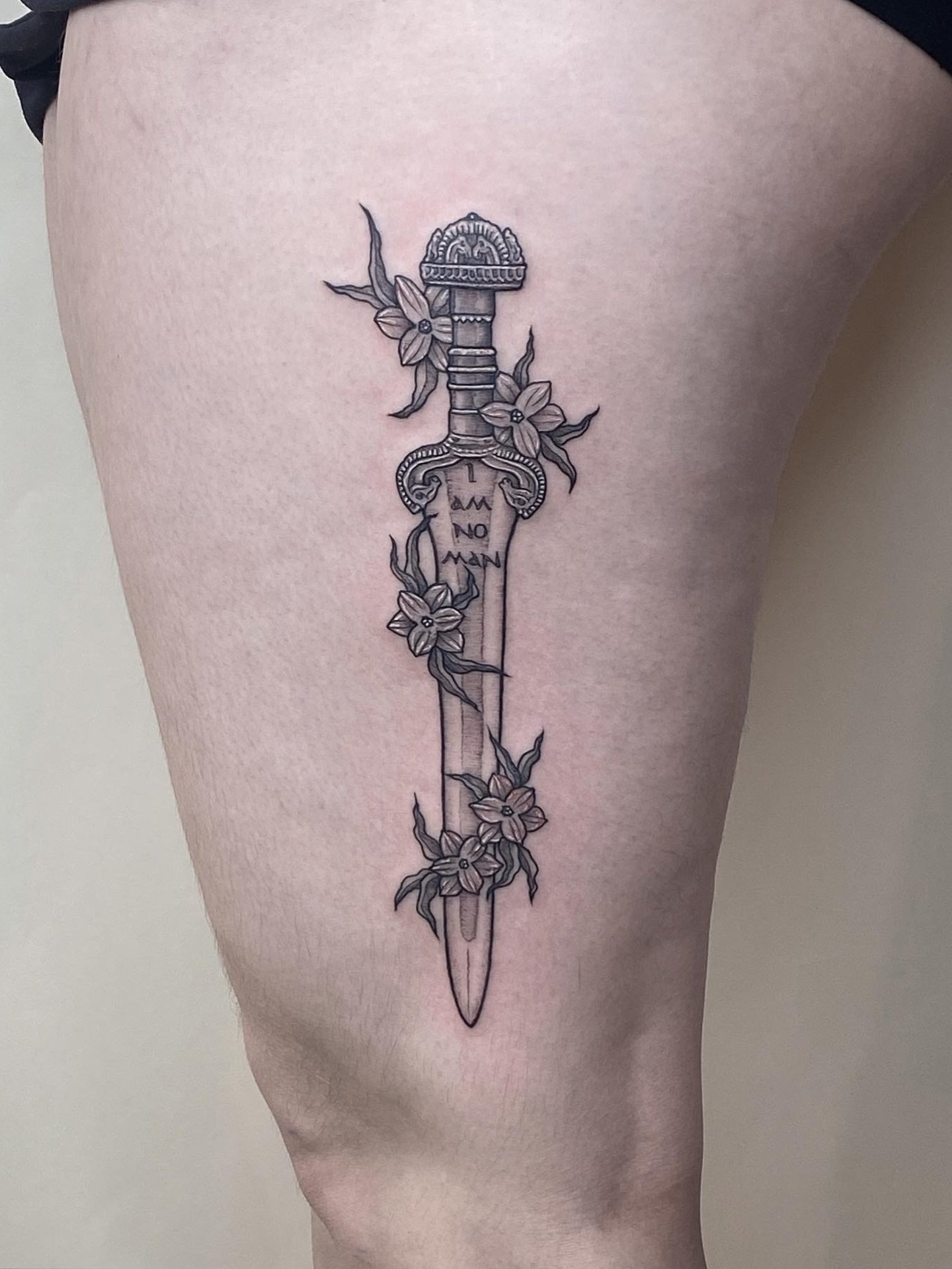 Sword with flowers black and grey tattoo on the thigh by Carmen Figueroa, New York, New York