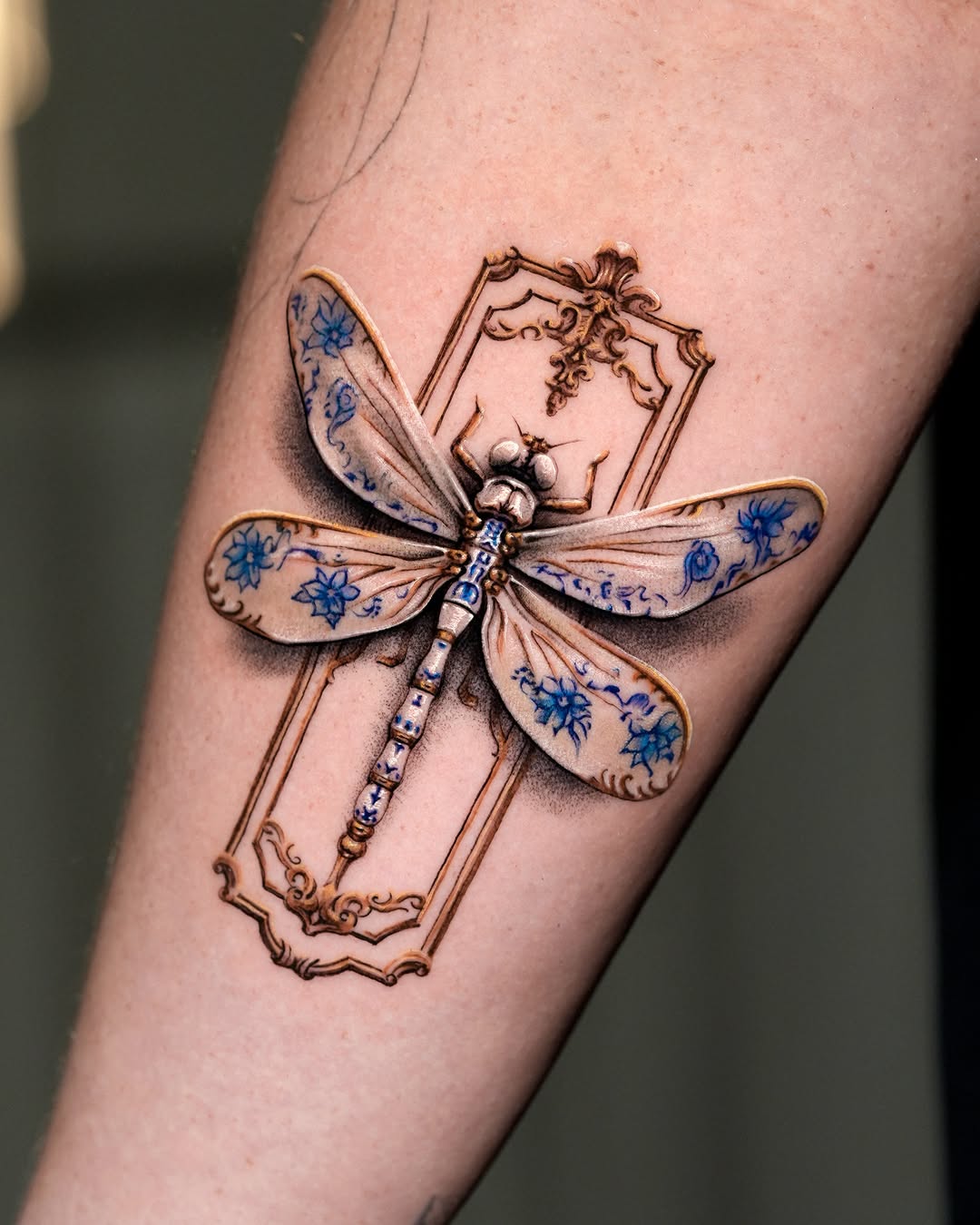 Dragonfly with ornate frame fine line tattoo on the forearm by Gody