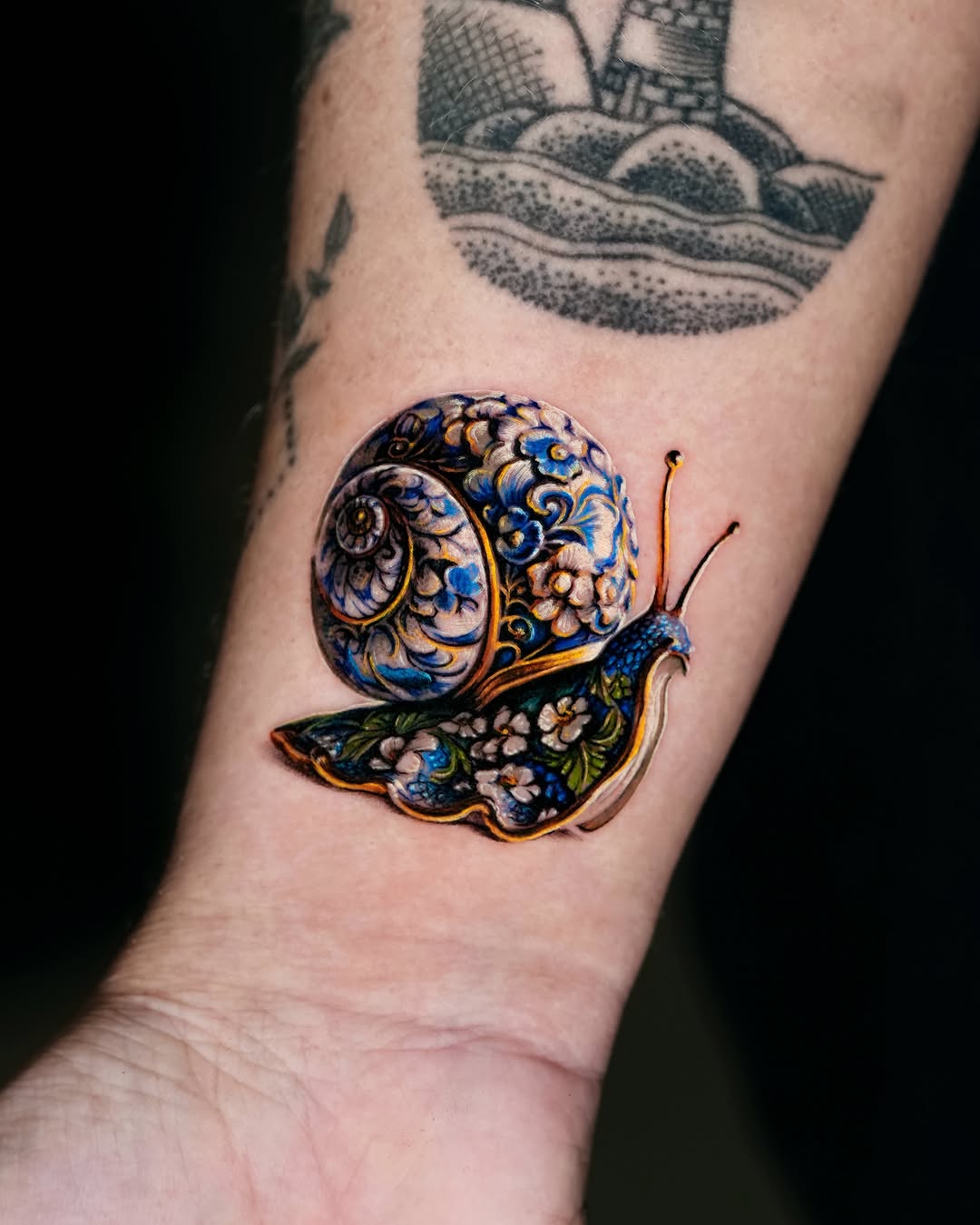 Ornate snail watercolor tattoo on the forearm by Gody