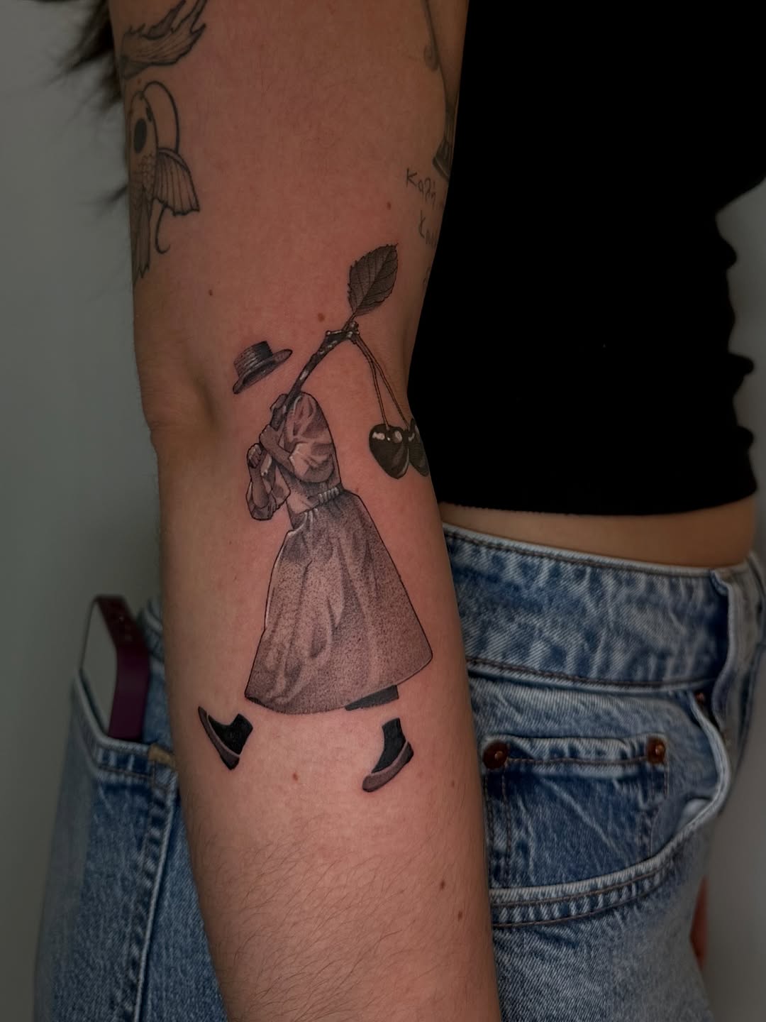 Figure carrying cherries surrealism tattoo on the forearm by 𝘋𝘪𝘢𝘯𝘯𝘢