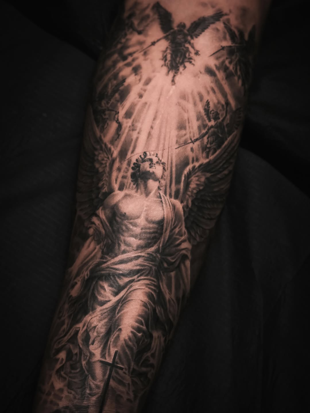 Angelic scene with a cross realism tattoo on the forearm by Pitasso tattoo black and grey