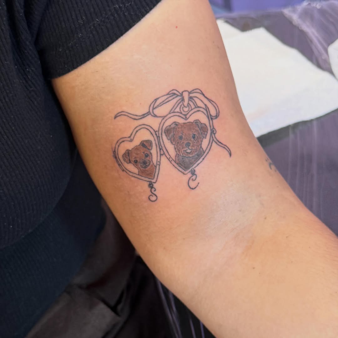 Two dogs in heart lockets realism tattoo on the forearm by Jay