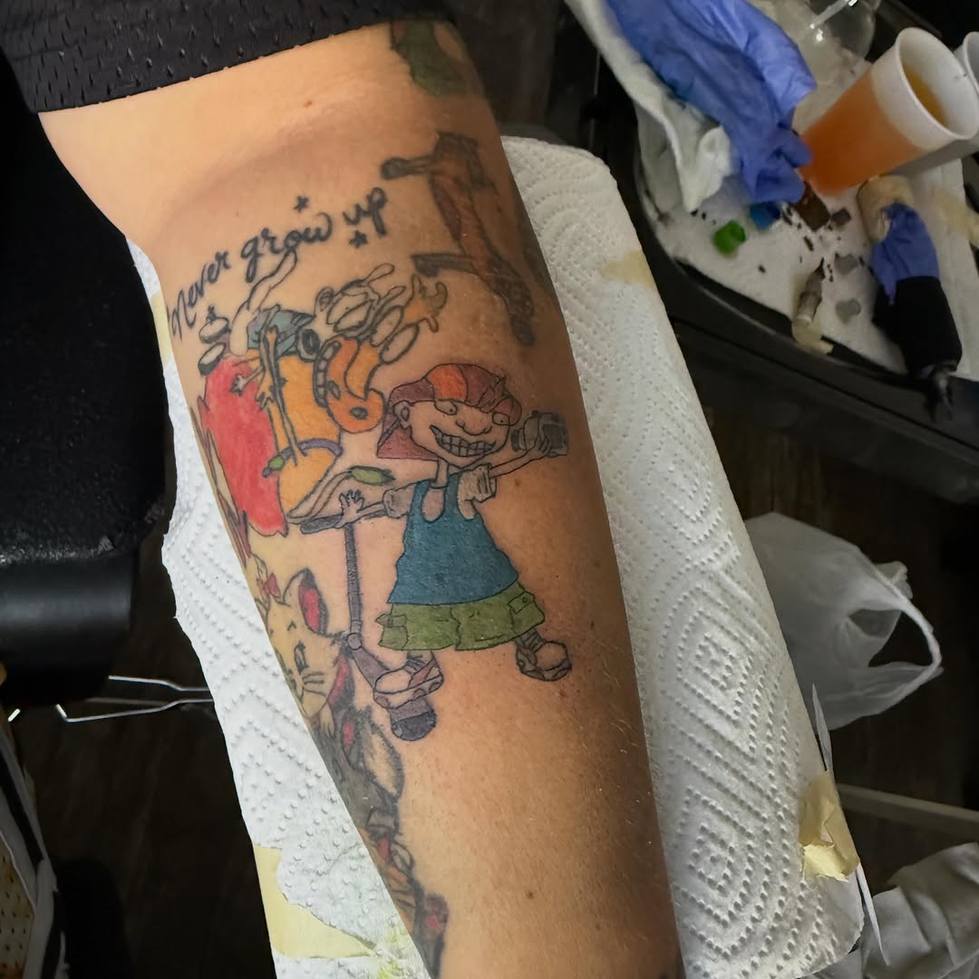 Cartoon character with text tattoo on the forearm by Jay