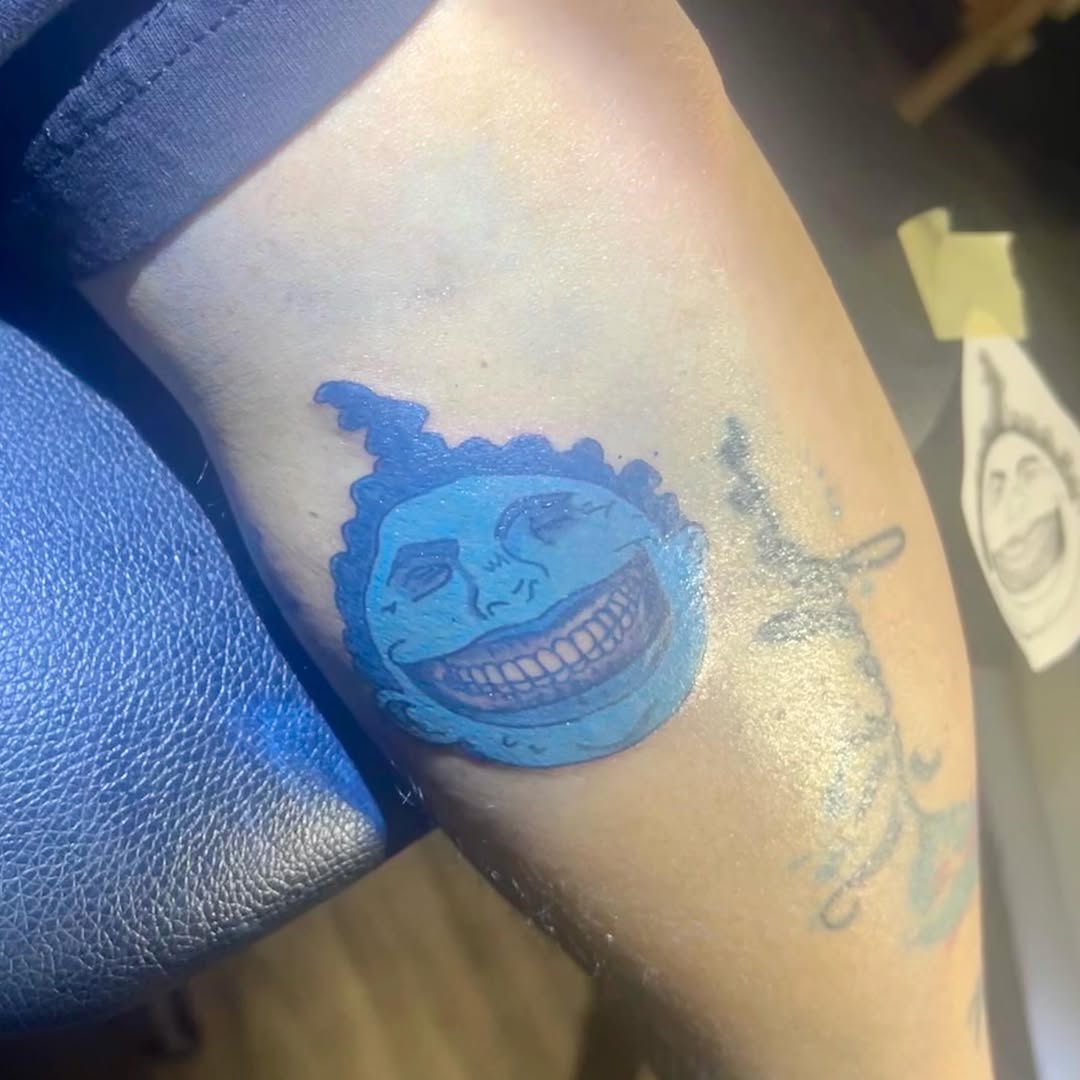 Blue moon face with wide smile tattoo on the forearm by Jay